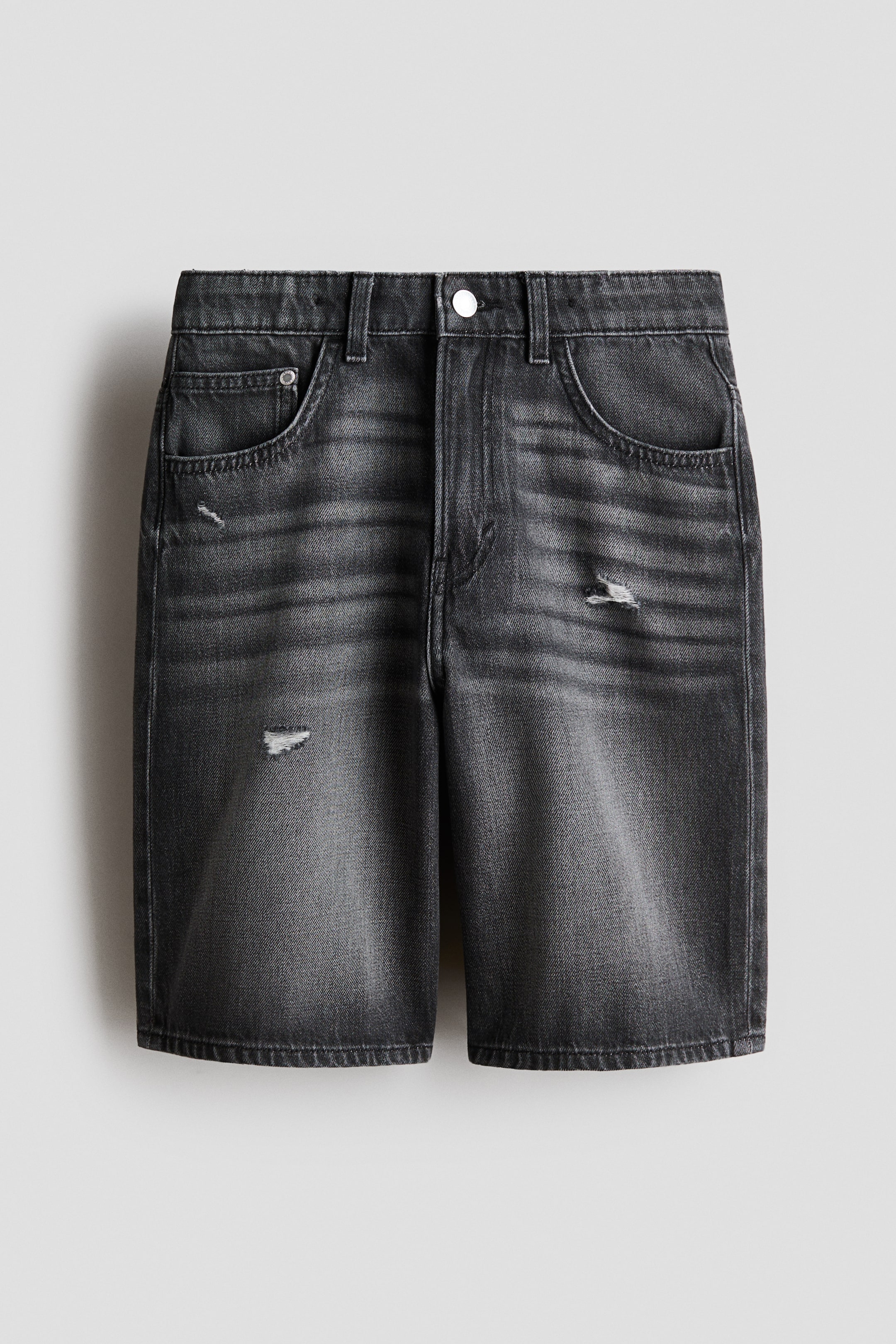View larger image: Knee-length, 5-pocket shorts in dark gray washed cotton denim are presenting from the front, featuring a loose fit through the hip and thigh with a dropped crotch and a waistband with belt loops. A silver button closure and zip fly are visible, along with two front pockets, a coin pocket, and distressed rips on the front of the thighs.