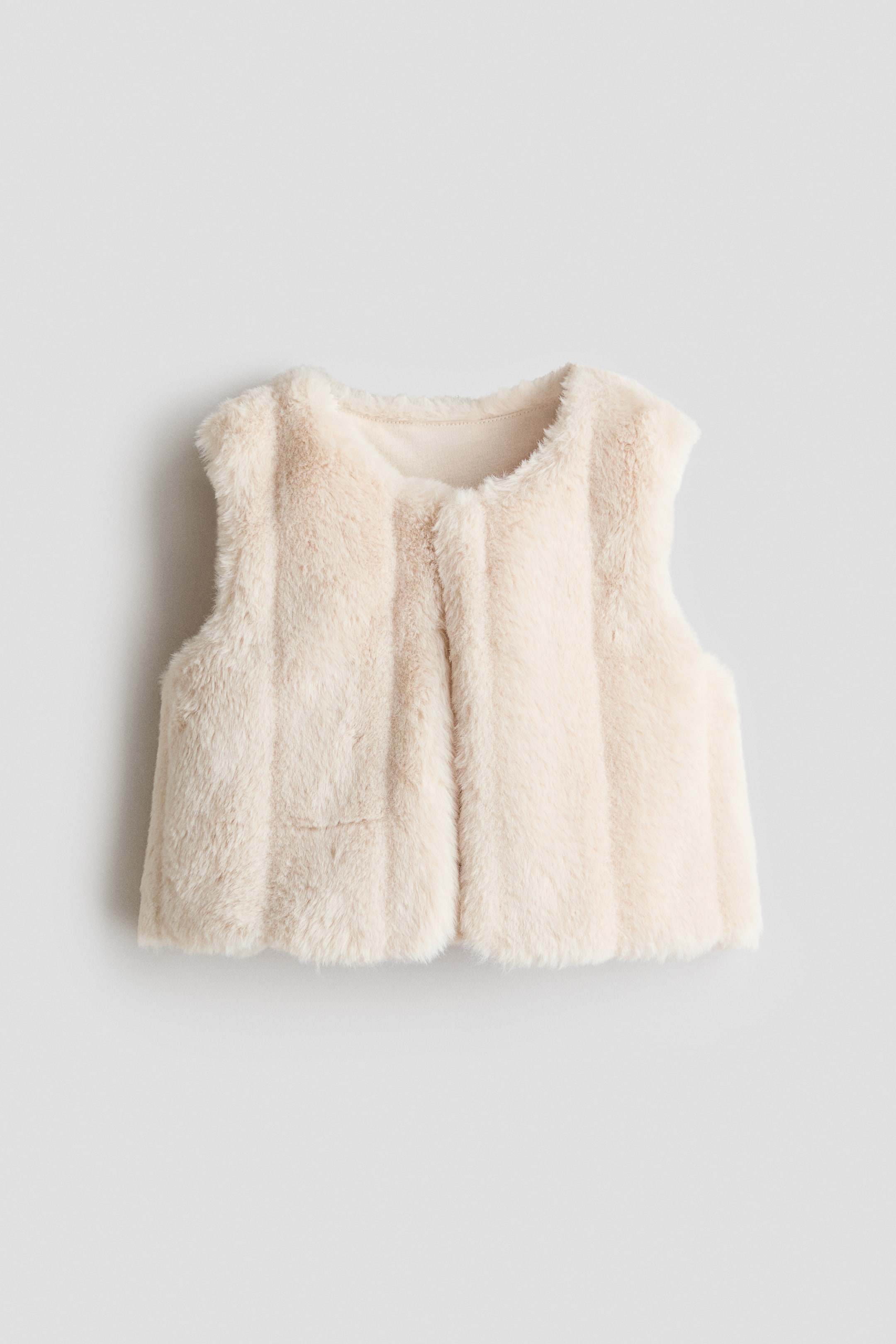 View larger image: A cream-coloured gilet is presented front-facing, showcasing its soft, fluffy fabric with subtle vertical paneling. It features a round neckline, a concealed button closure at the top, and a jersey lining visible along the neck and armhole edges.