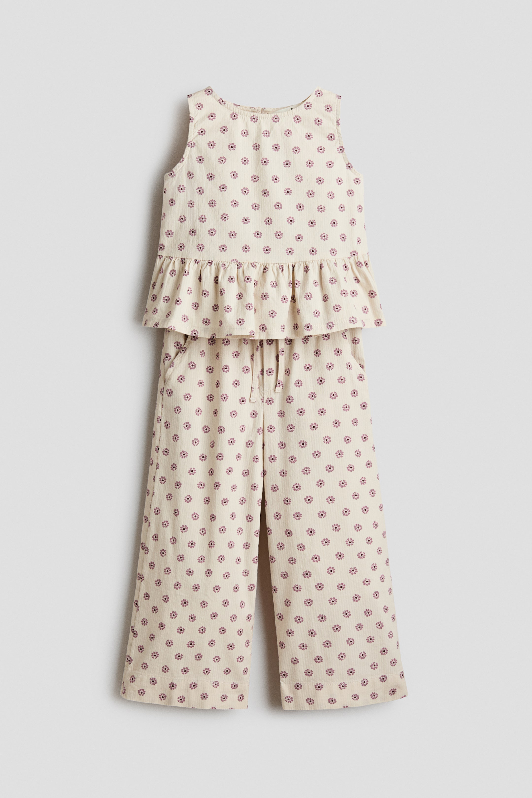 View larger image: A front-facing clothing set features a sleeveless top with a round neckline and a peplum, paired with wide-leg trousers. Both pieces are made from a light-colored cotton seersucker fabric with a repeating pattern of small maroon flowers, and the trousers are designed with an elastic drawstring waist.