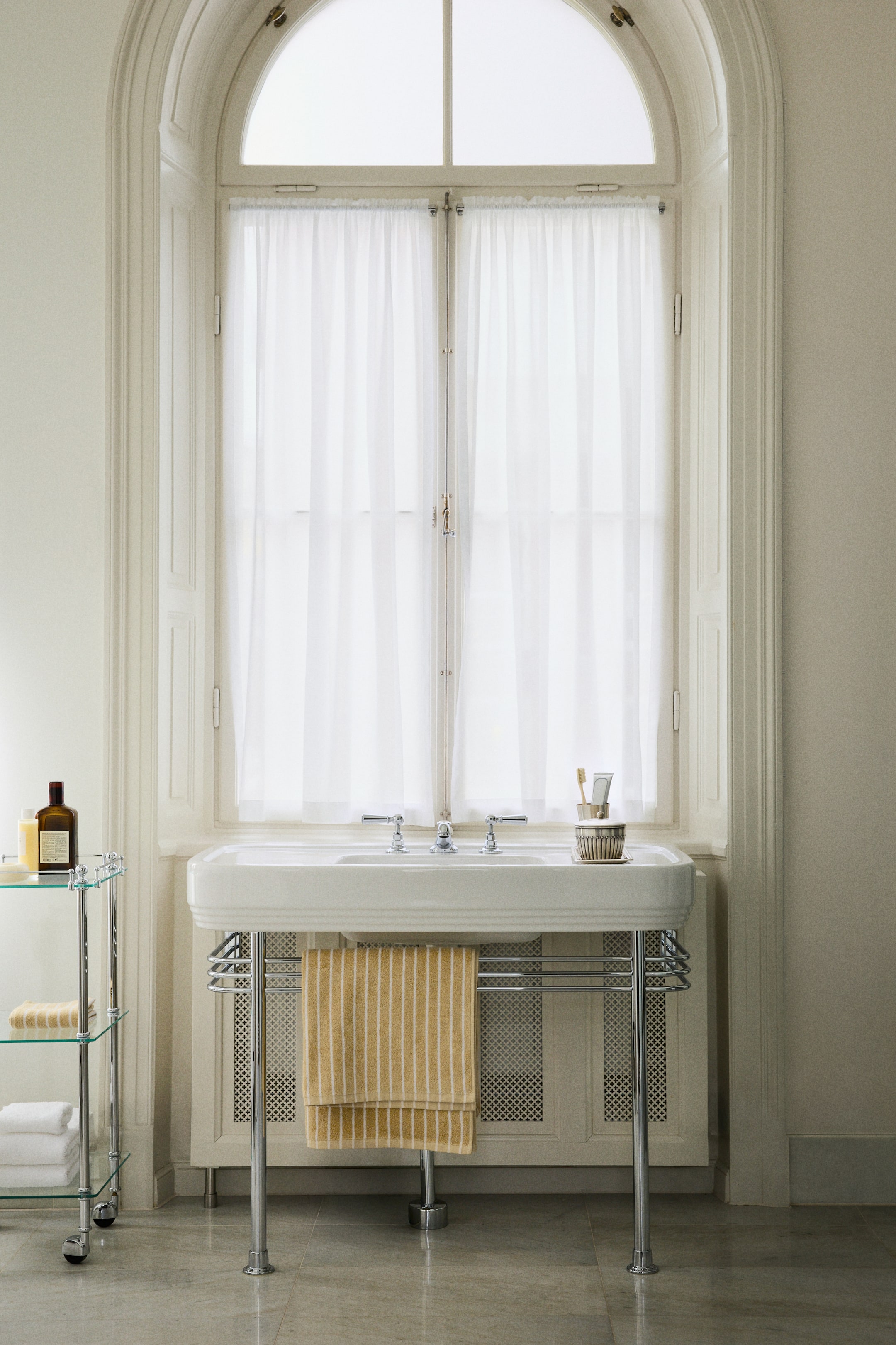 Se større billede: Et gult badehåndklæde med tynde hvide lodrette striber hænger foldet over en metalhåndklædestang.