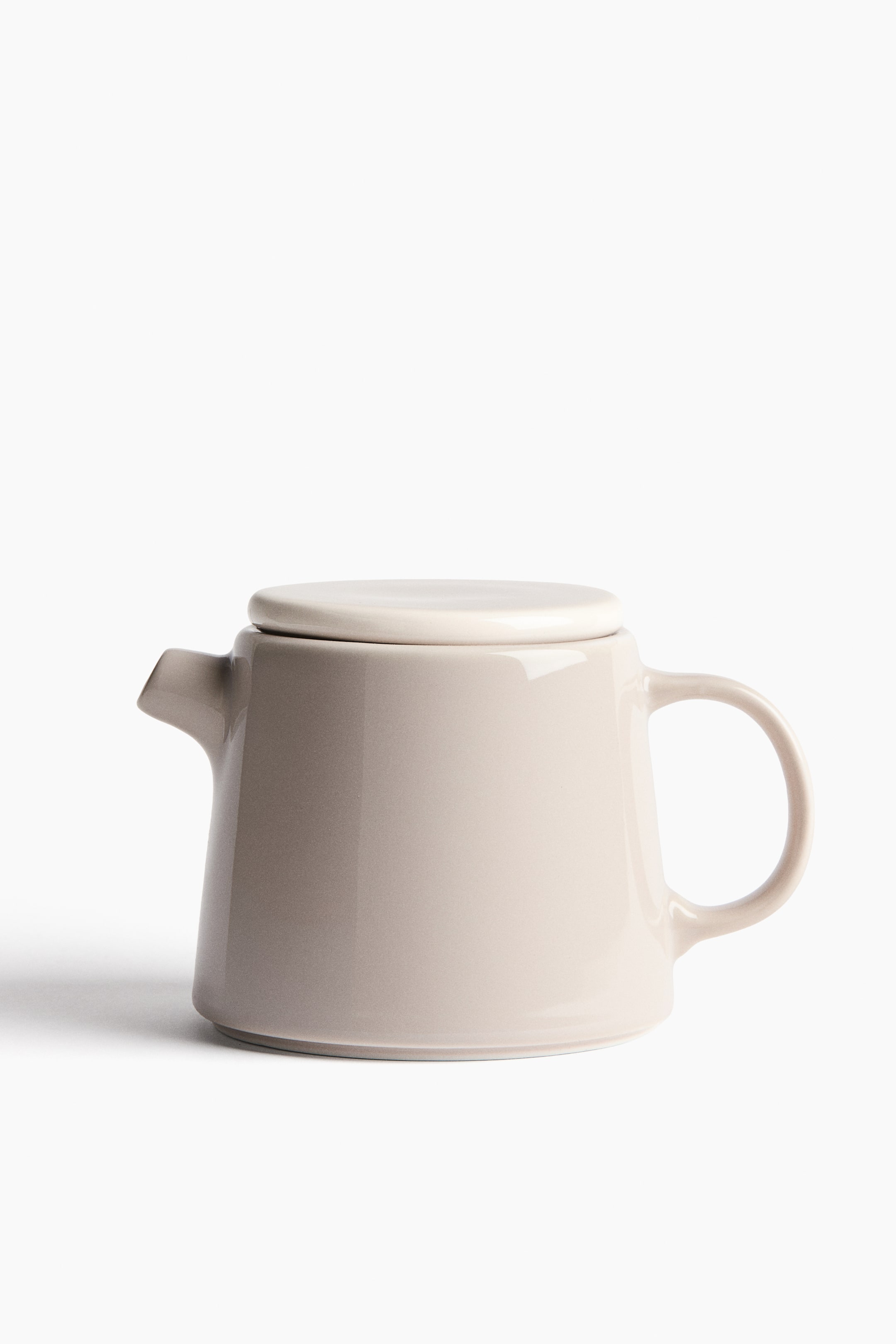 View larger image: A light taupe ceramic teapot features a tapered body, with a short triangular spout extending from its left side. A curved C-shaped handle is positioned on its right side, and a flat circular lid, slightly lighter in tone, rests on top.