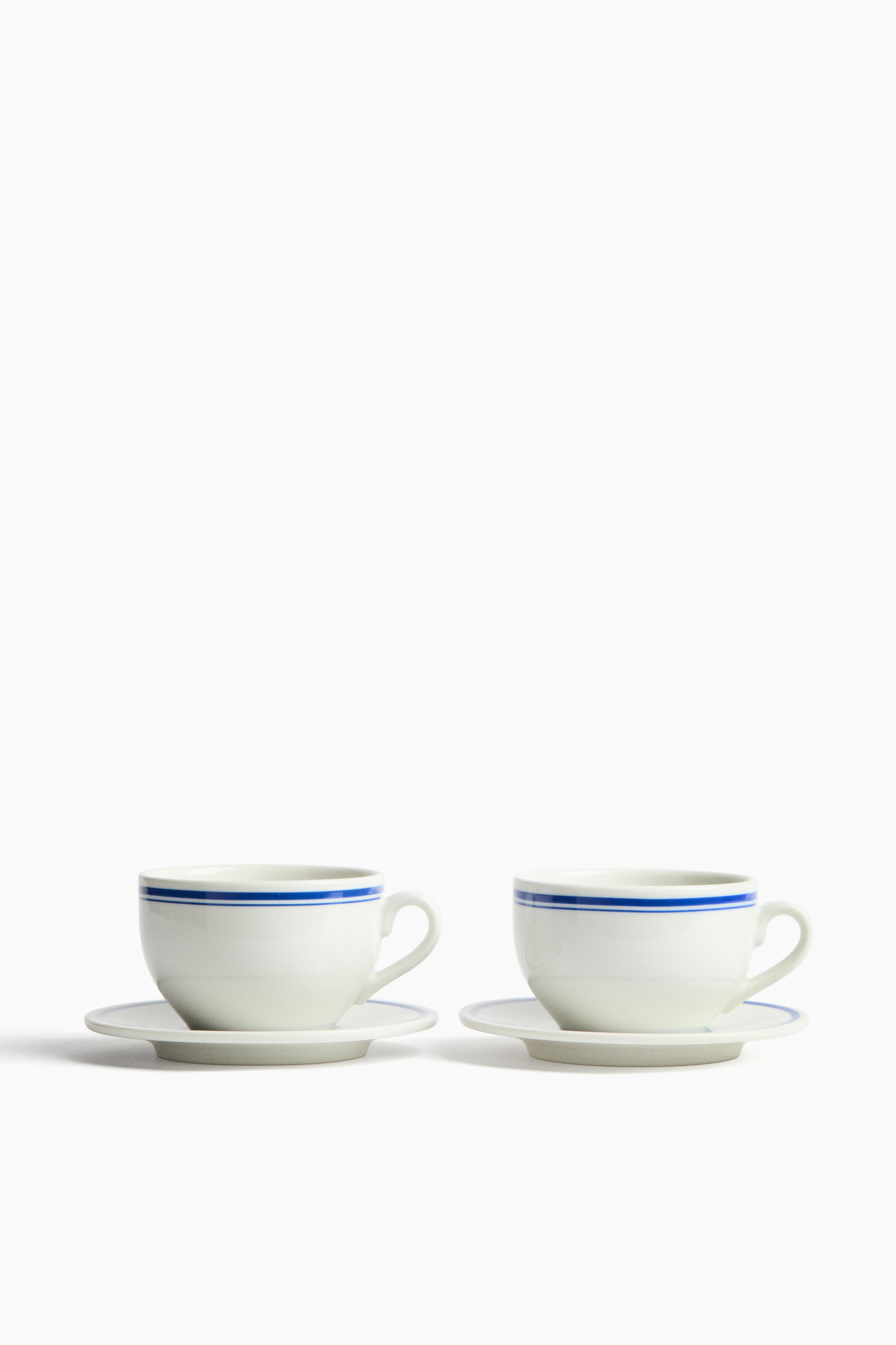 拡大画像を表示: 2つの磁器製カップとソーサーには、各カップの上部縁に2本の青い水平ストライプが描かれ、各ソーサーには1本の青い水平ストライプが施されています。正面を向いた状態で展示されています。
