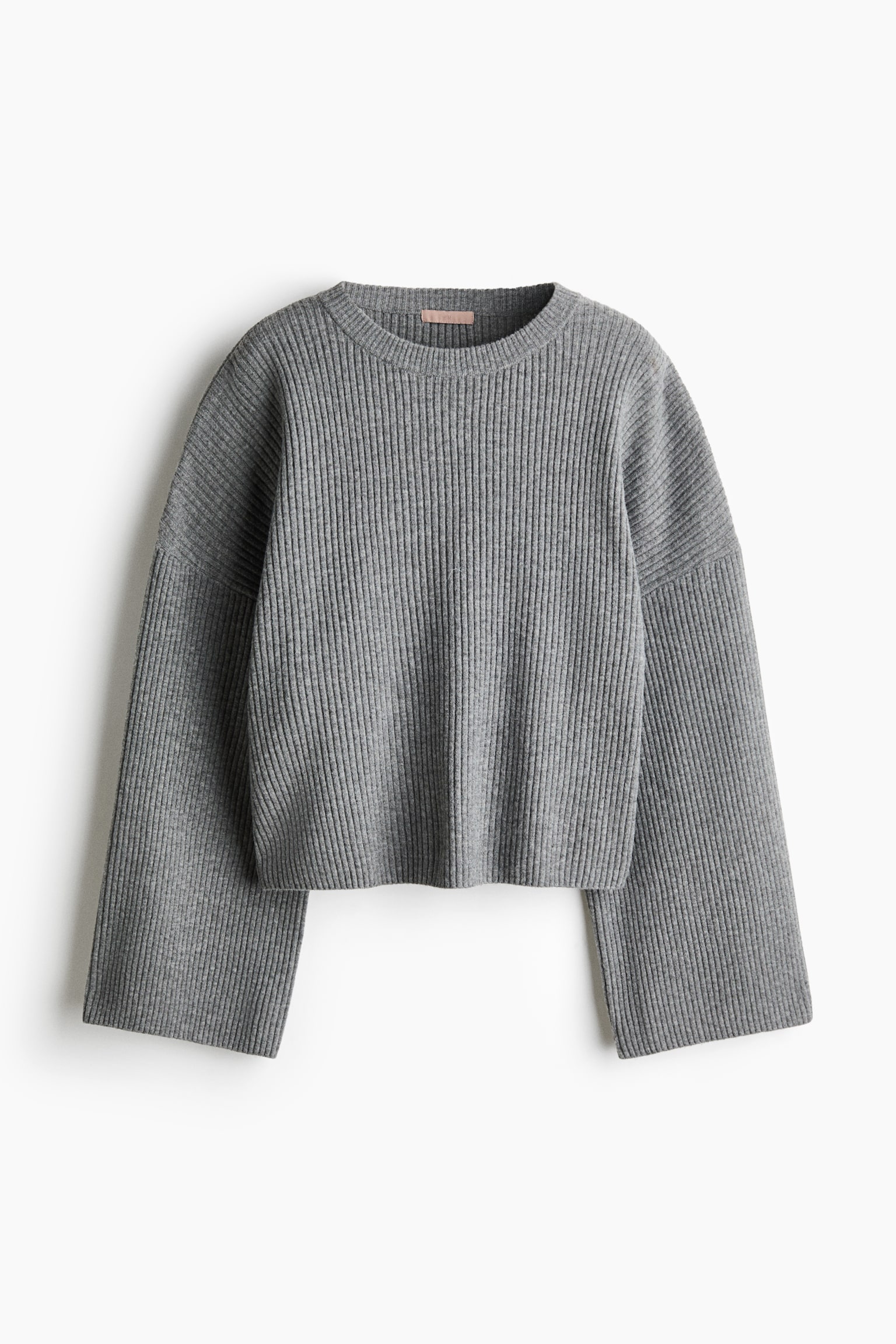 Un jersey gris de corte oversize en suave punto canalÃ© cuelga visto de frente, mostrando un cuello redondo acanalado, hombros caÃ­dos y mangas largas y anchas.