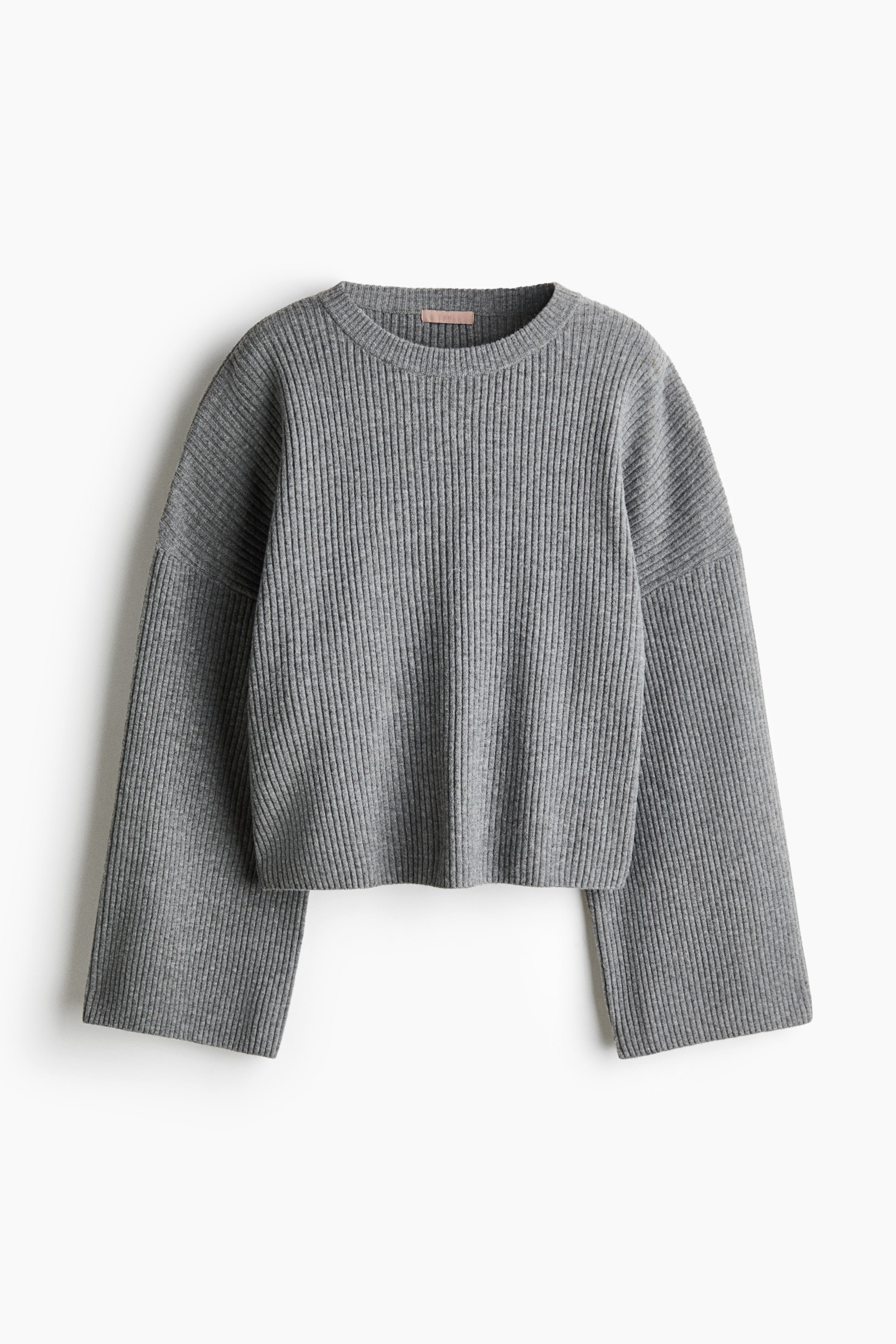 Größeres Bild anzeigen: Ein oversized grauer Pullover aus weichem Rippstrick hängt in frontaler Ansicht und zeigt einen gerippten Rundhalsausschnitt, tief angesetzte Schultern und lange, weite Ärmel.