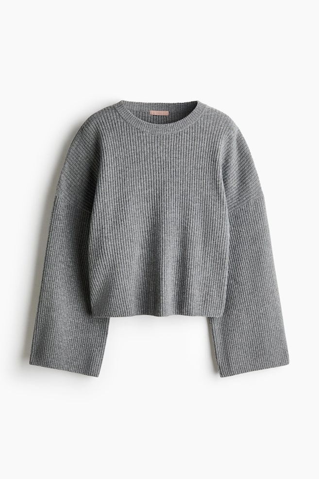 An oversized grey sweater in a soft rib knit is hanging from a front-facing angle, displaying a ribbed crew neck, low dropped shoulders, and long, wide sleeves. - 1