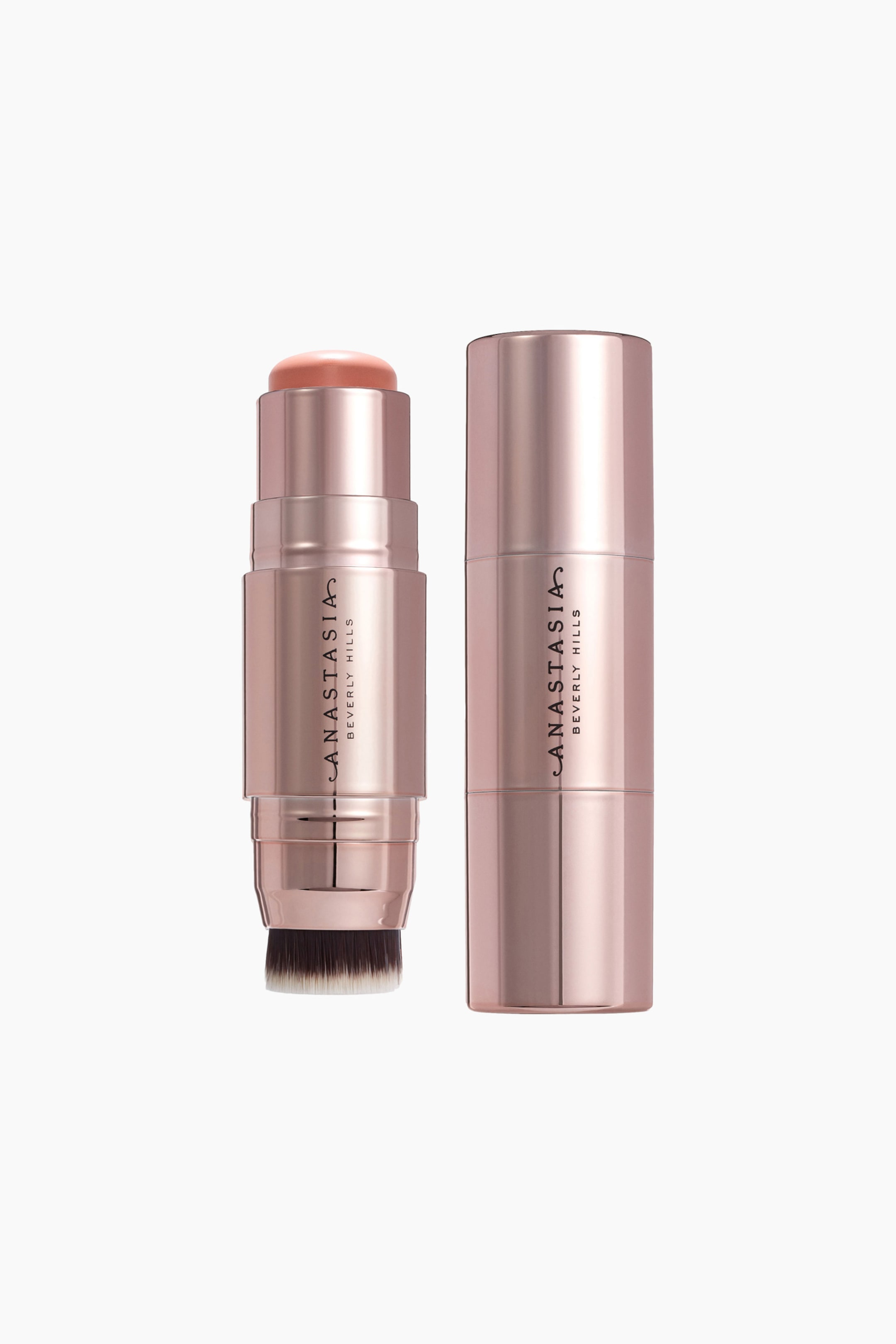 Näytä suurempi kuva: Kaksi metallinhohtoista ruusukultaisen sävyistä meikkipuikkoa seisoo pystyssä, ja molemmissa on "Anastasia Beverly Hills" -logo. Toinen puikko on auki, ja sen yläosassa näkyy persikanpunainen vaaleanpunainen kupolimainen tuote sekä alareunassa meikkisivellin, jossa on tummat ja valkoiset harjakset; toinen puikko näyttää olevan suljettuna.