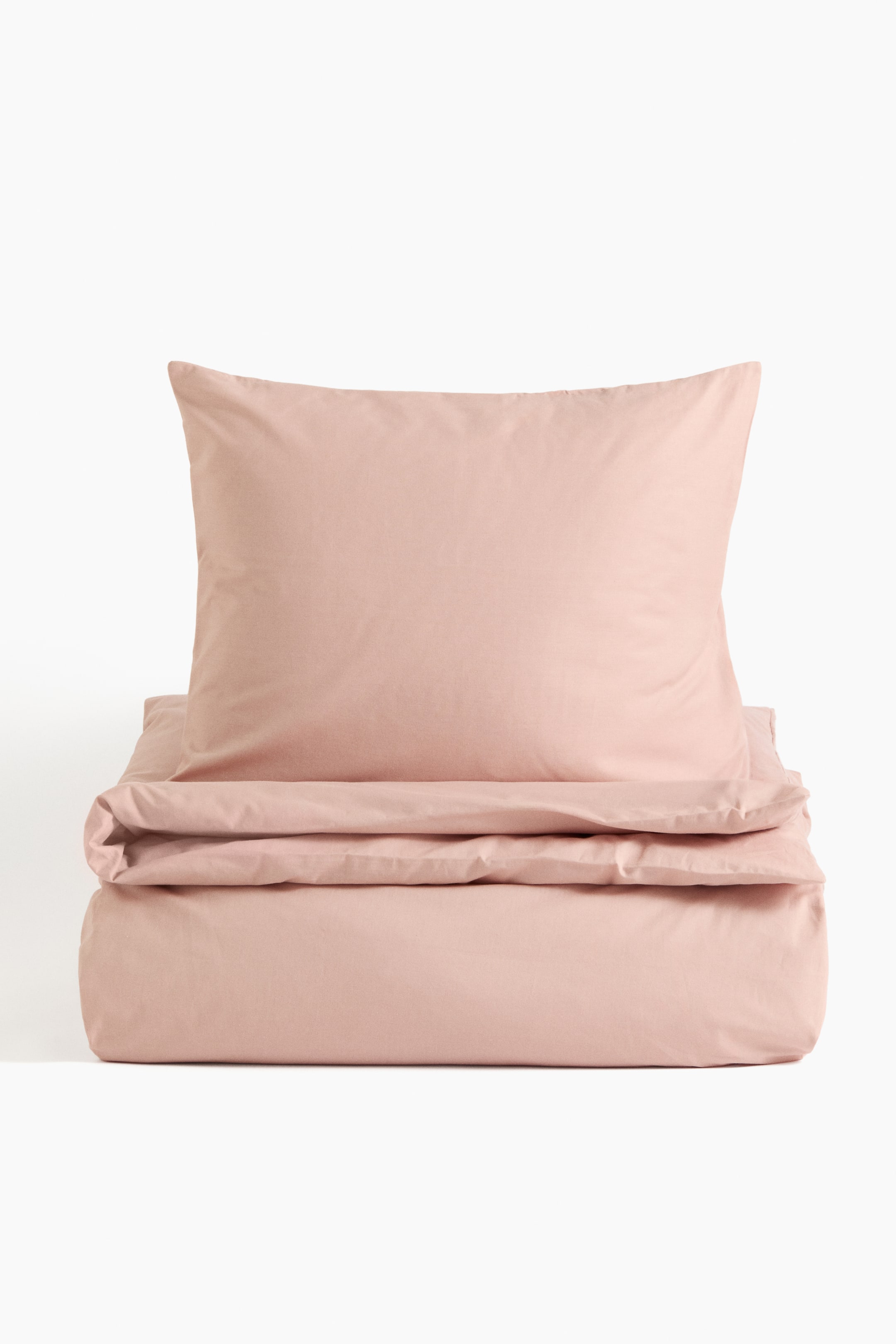 View larger image: A single duvet cover set is showcasing its front, with one blush pink pillowcase positioned upright behind a neatly folded blush pink duvet cover. Both items exhibit a smooth fabric texture.