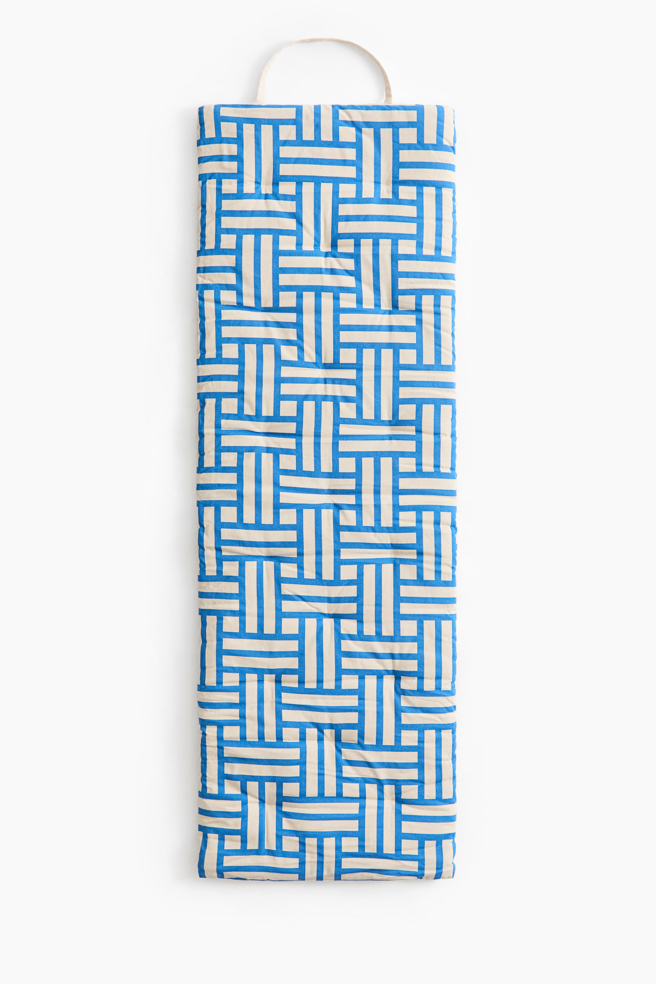 Se større billede: En polstret strandmadras med et blåt og cremefarvet geometrisk mønster af sammenflettede striber, der fremstår i en kompakt, aflang form med et stofhåndtag i den ene ende.