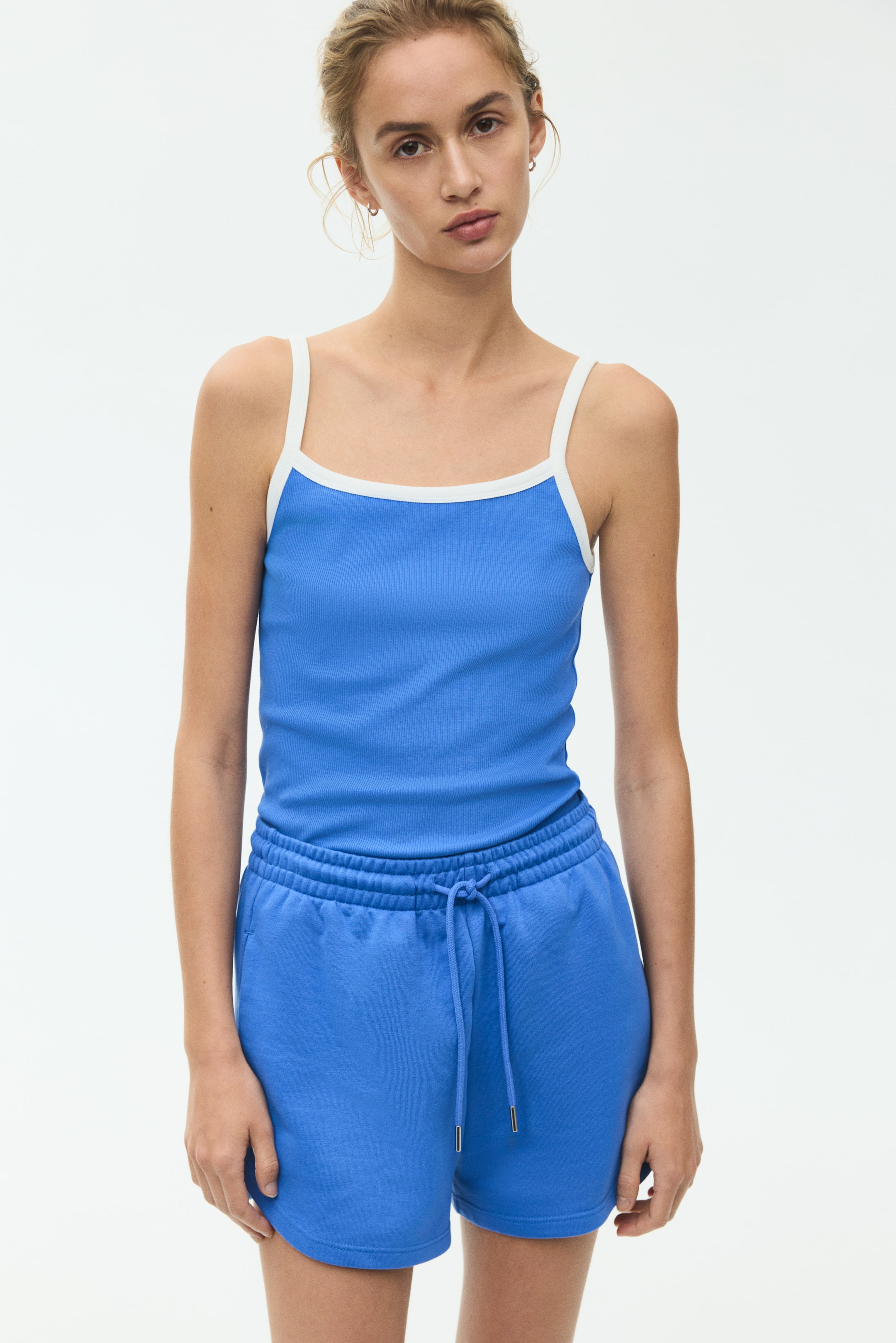 View larger image: The model is wearing a fitted top made from blue ribbed cotton jersey, showcasing a scoop neckline and slim shoulder straps with white contrast binding.