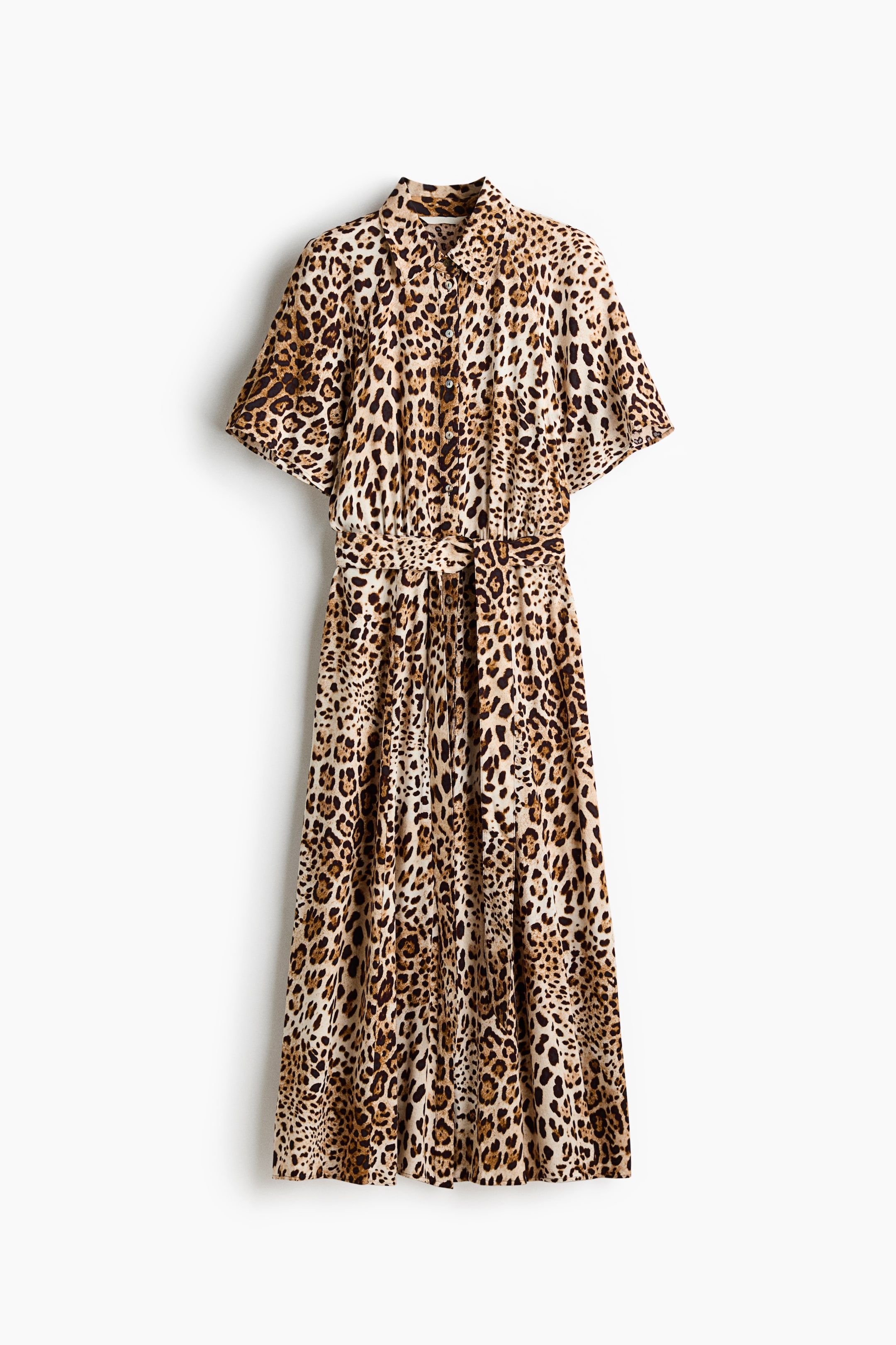 Visa större bild: En vadlång klänning i leopardmönstrat vävt tyg visas framifrån, med en krage, knappar längs framsidan och korta raglanärmar. Midjepartiet är designat med smal resår baktill och rynkor framtill och baktill, medan ett avtagbart knytbälte är knutet framtill.