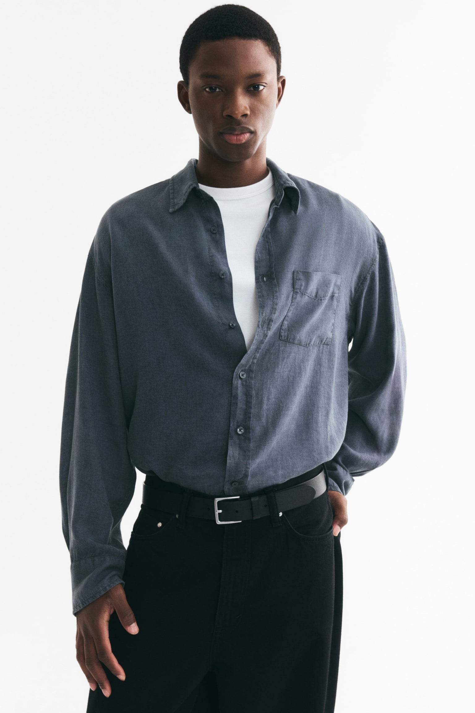 A charcoal grey shirt is facing front, showcasing its relaxed fit. It features a pointed collar, long sleeves with buttoned cuffs, a full button-front with dark buttons, and a single patch pocket on the left chest. - 1