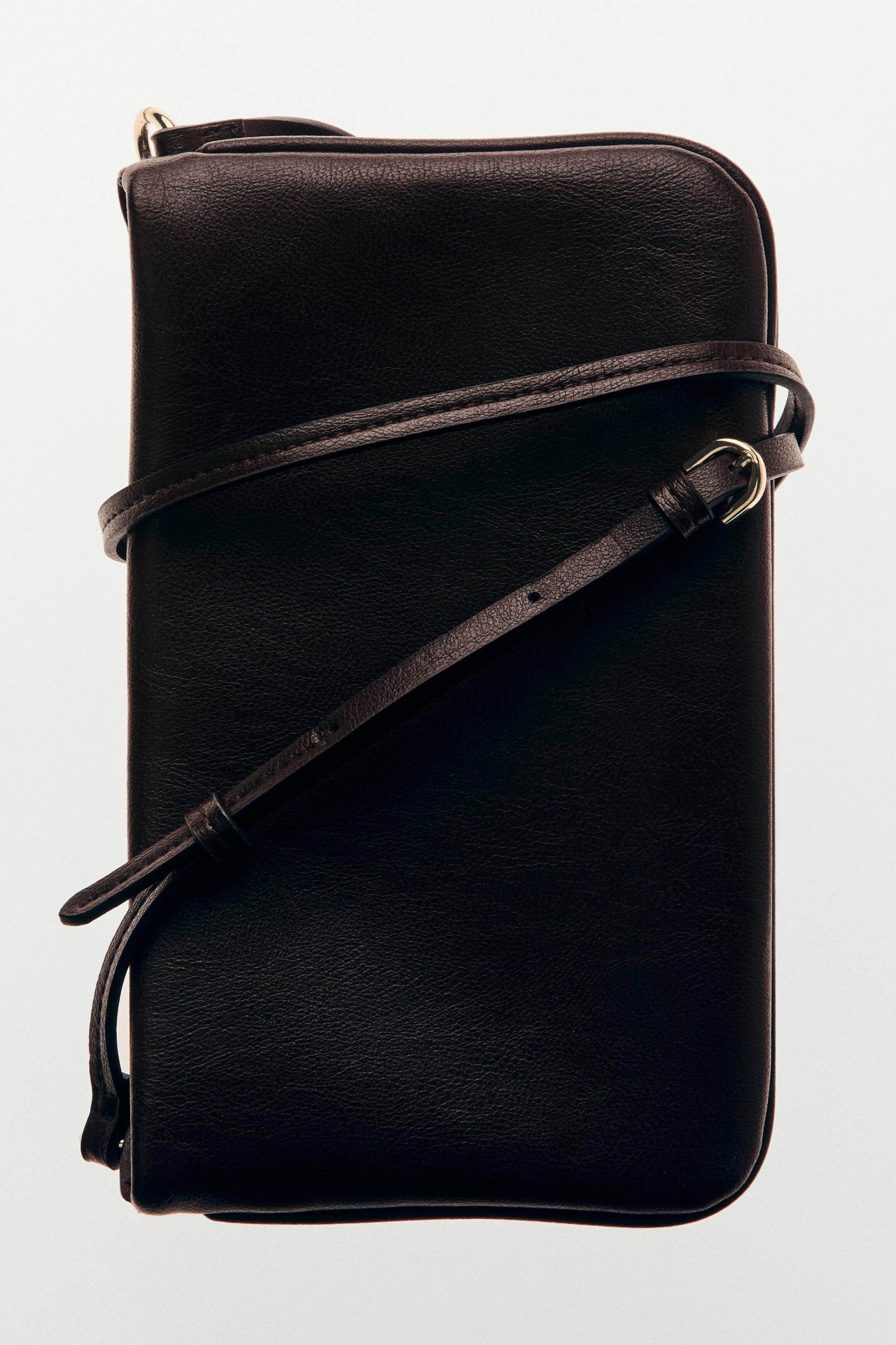 Ver imagen más grande: Un bolso bandolera marrón oscuro está de frente, mostrando su material texturizado y una correa de hombro estrecha y ajustable con una hebilla dorada. El bolso cuenta con un compartimento abierto y un compartimento con cremallera.