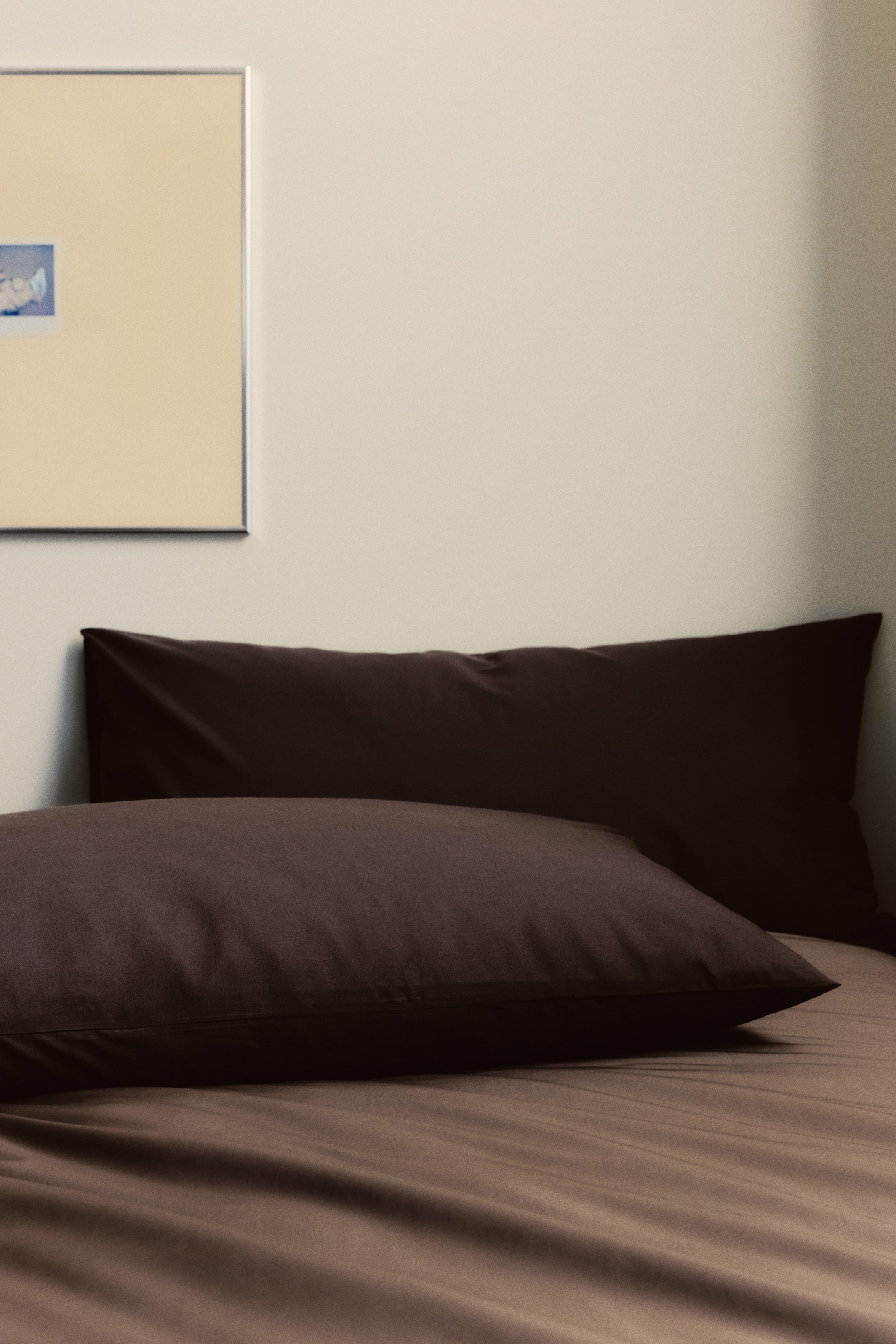 Agrandir l'image: Une paire de taies d'oreiller marron foncé en tissage de coton doux est visible, avec la taie d'oreiller avant inclinée vers le spectateur et montrant une ouverture en enveloppe sur le côté. Une taie d'oreiller plus longue est positionnée horizontalement derrière elle.