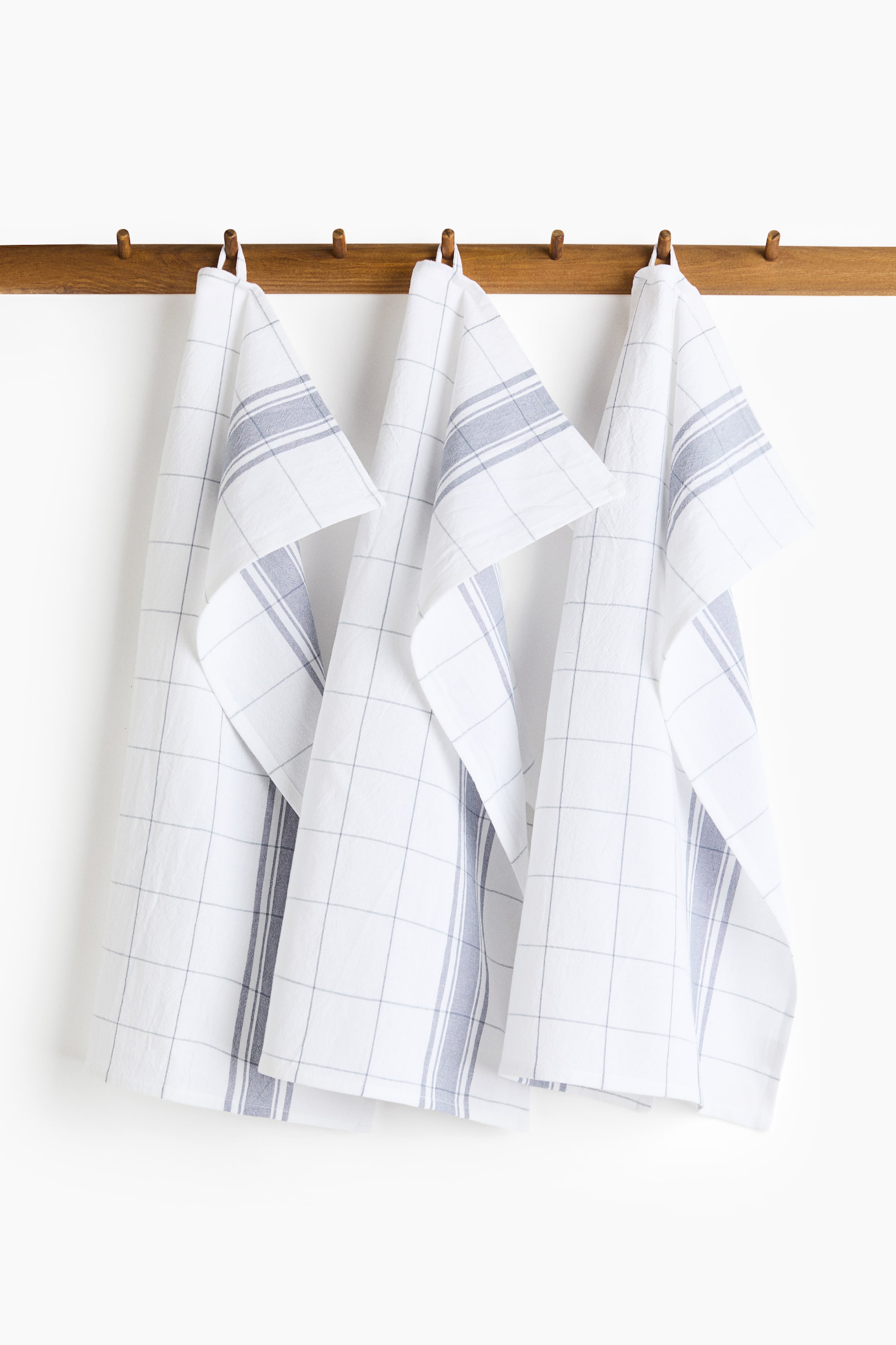 View larger image: Three cotton tea towels are hanging, each showcasing a distinct grey and white pattern. Each towel features horizontal grey stripes at the top, transitioning into a fine grey grid, and includes a hanging loop on one short side.