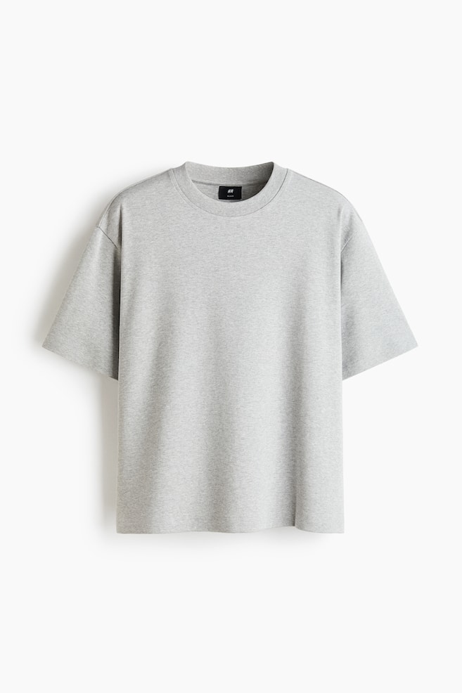 "The light grey heathered t-shirt is shown from the front, highlighting its ribbed crew neck and short, dropped-shoulder sleeves. Inside the back of the neckline, a black brand label is visible. The t-shirt offers a relaxed fit." - 1