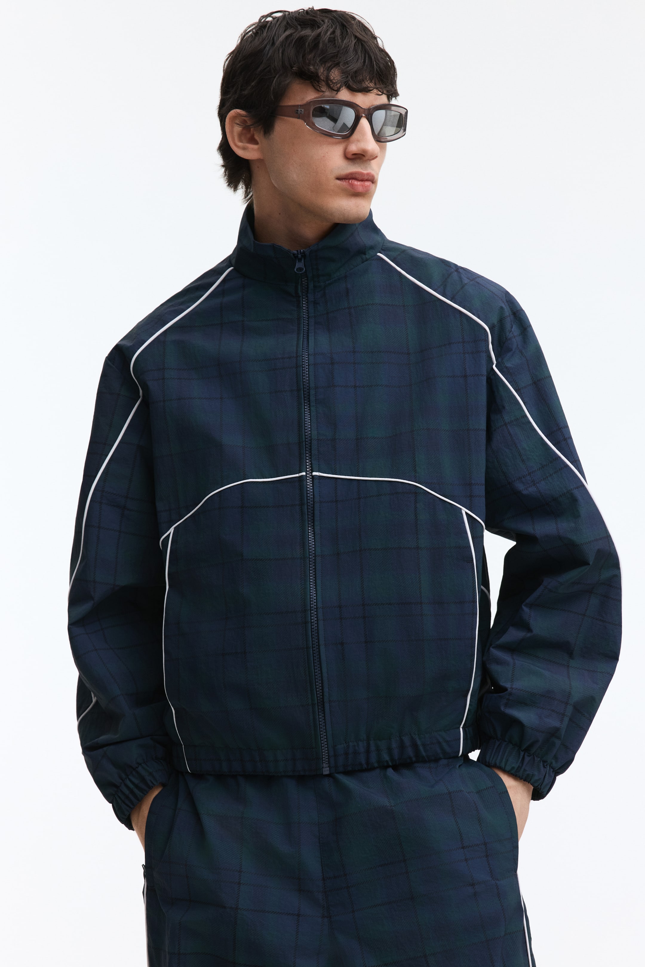 View larger image: The plaid jacket showcases a dark blue and green tartan pattern, highlighted by white piping along the shoulders, down the sleeves, and across the chest. It features a full-zip closure, a stand-up collar, and elasticized cuffs and hem. The look is completed with matching plaid pants.