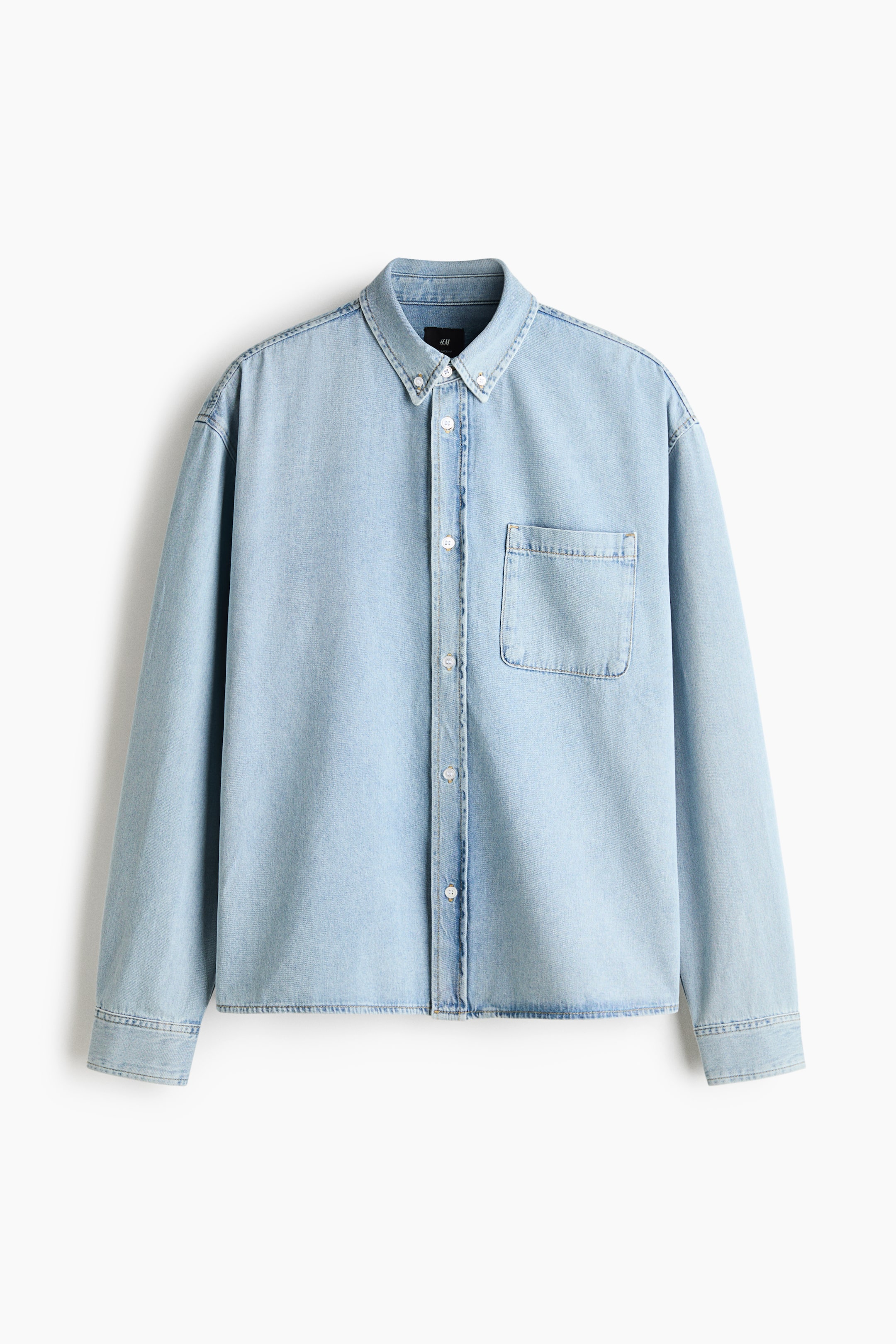 Größeres Bild ansehen: Ein hellblaues Jeanshemd hängt frontal und verfügt über einen Button-down-Kragen, eine durchgehende Knopfleiste und eine einzelne aufgesetzte Brusttasche auf der linken Brust. Das Hemd zeigt lange Ärmel mit geknöpften Manschetten und einen geraden Saum.