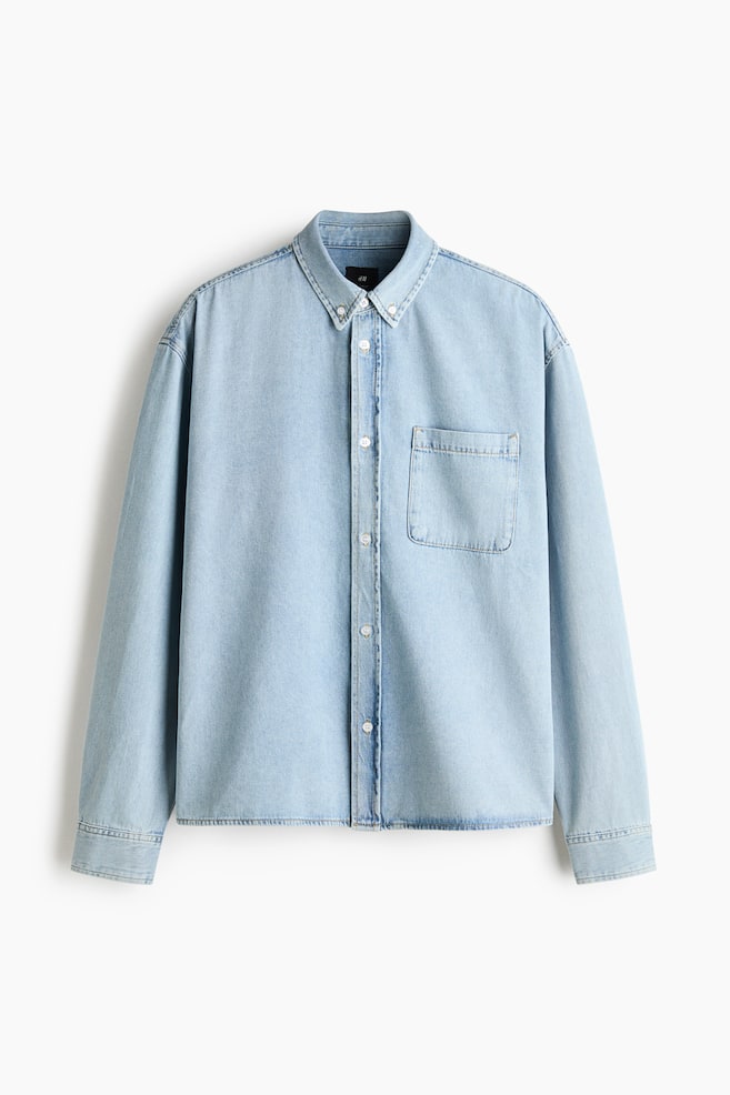 Ein hellblaues Jeanshemd hängt frontal und verfügt über einen Button-down-Kragen, eine durchgehende Knopfleiste und eine einzelne aufgesetzte Brusttasche auf der linken Brust. Das Hemd zeigt lange Ãrmel mit geknöpften Manschetten und einen geraden Saum. - 1