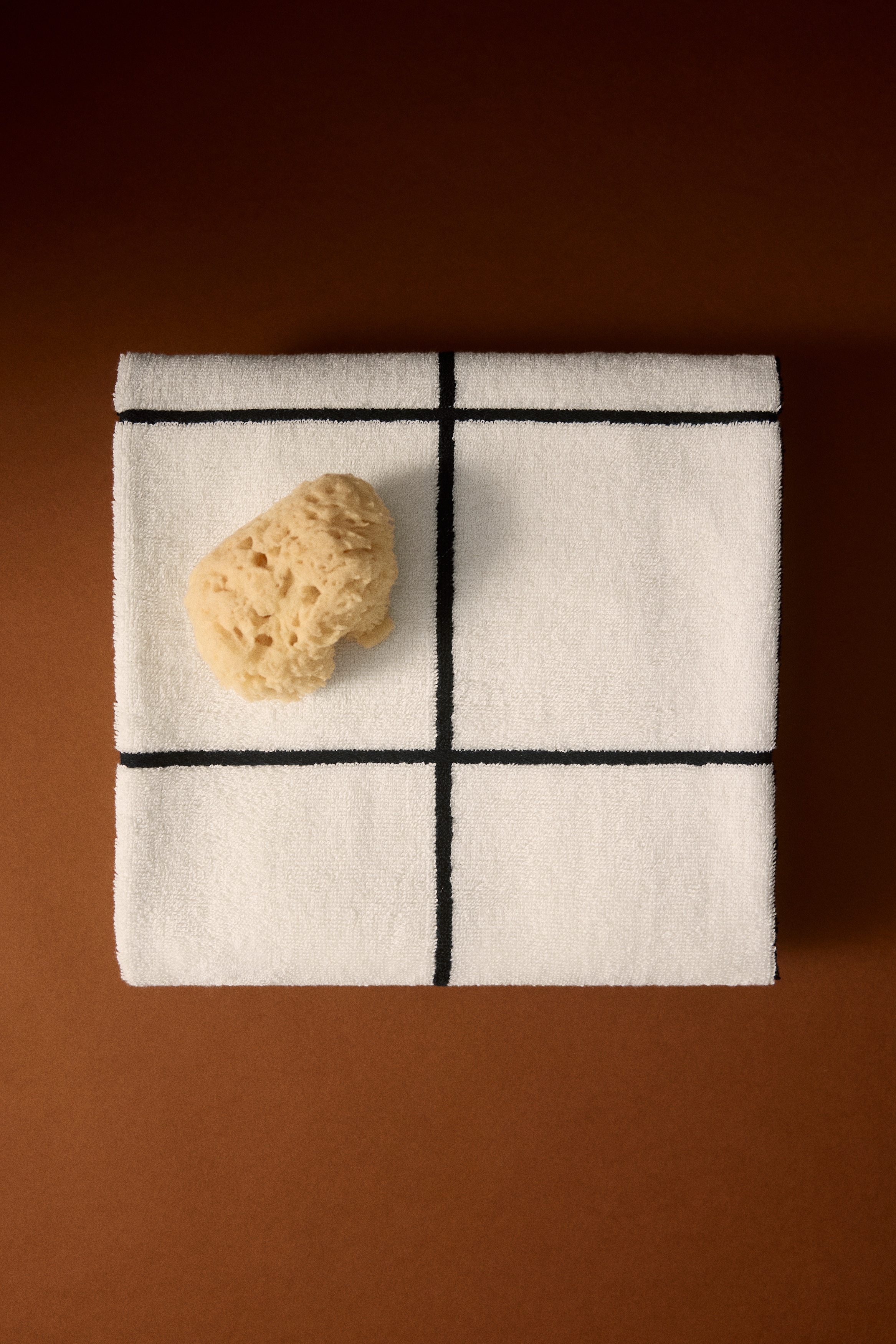 Un asciugamano color crema con un motivo a griglia nera irregolare è appeso a un piccolo gancio nero.