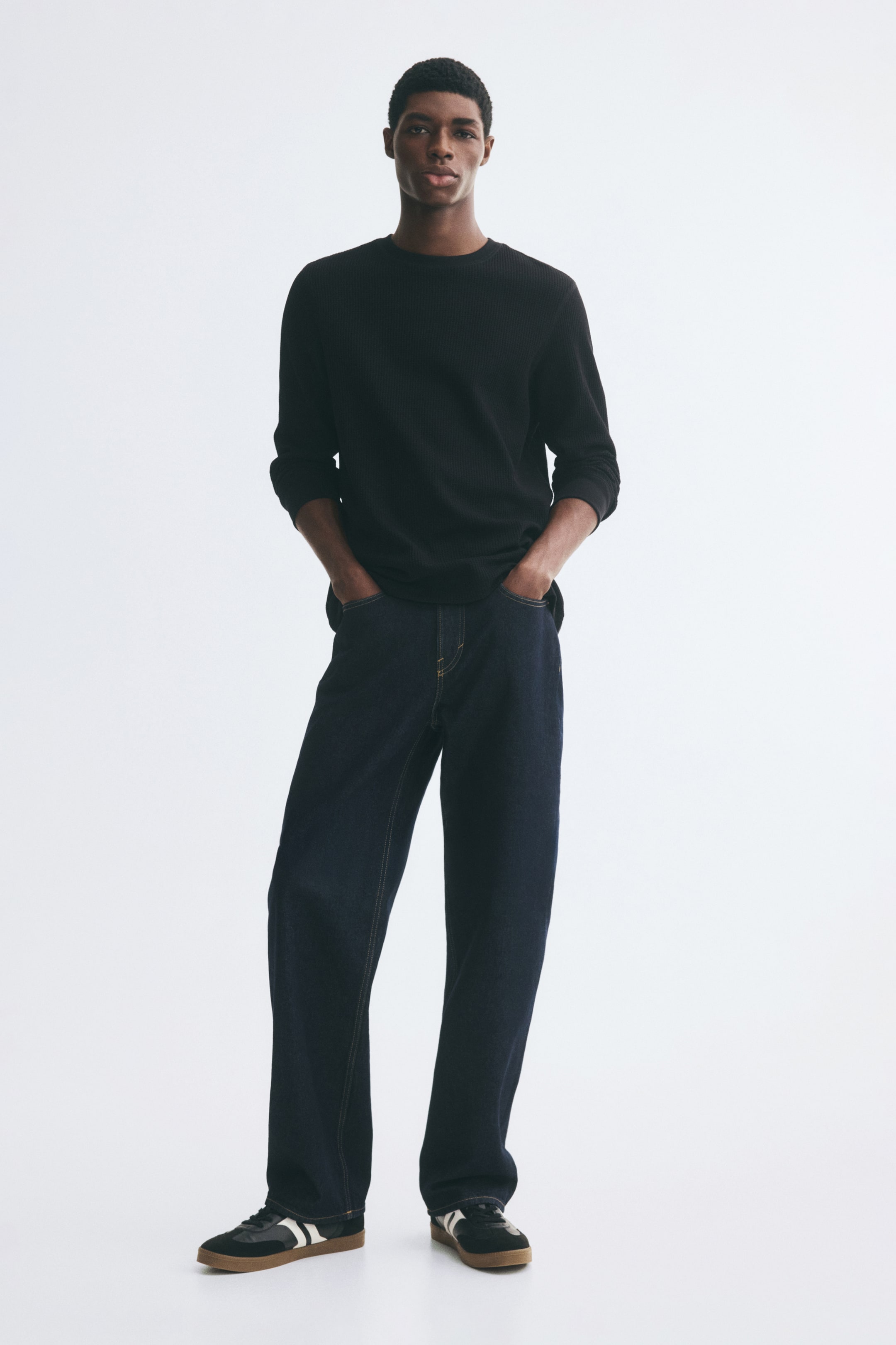 View larger image: A black long-sleeve tee in a waffled cotton-blend jersey is worn by the model, featuring a regular fit, a round neckline, and ribbed cuffs. The tee is styled with dark denim jeans and low-top sneakers.
