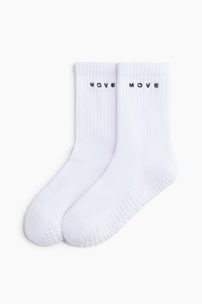 A pair of white, fine-knit sports socks is presented front-facing, featuring ribbed shafts with black "MOVE" embroidery and anti-slip protectors across the soles. - 1