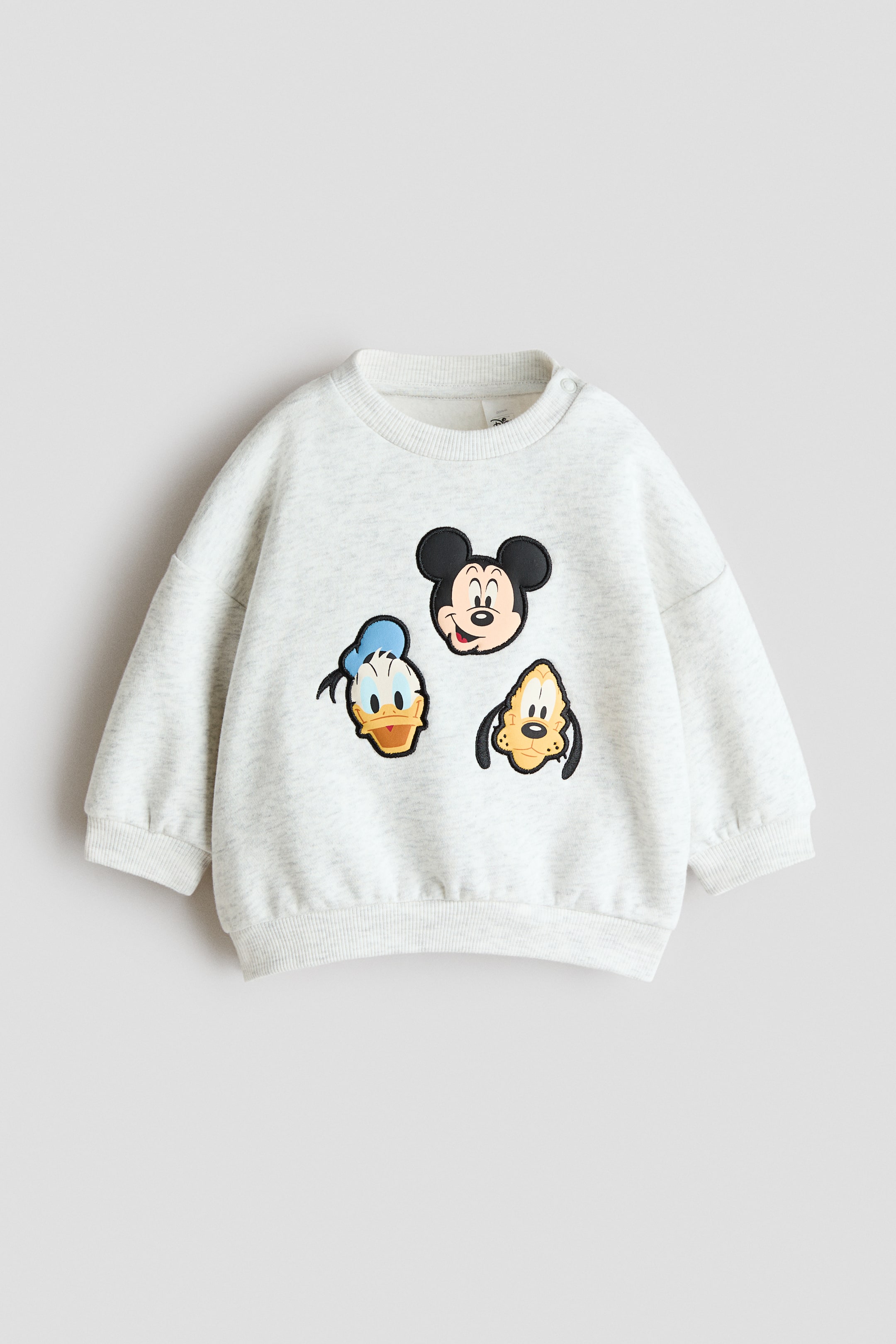 View larger image: The light grey marl sweatshirt is shown from the front, boasting a ribbed crew neck, long sleeves, ribbed cuffs, and a ribbed hem. Three appliquéd character faces, Mickey Mouse, Donald Duck, and Pluto, adorn the front, with two snap buttons securing the left shoulder of the ribbed neckline.