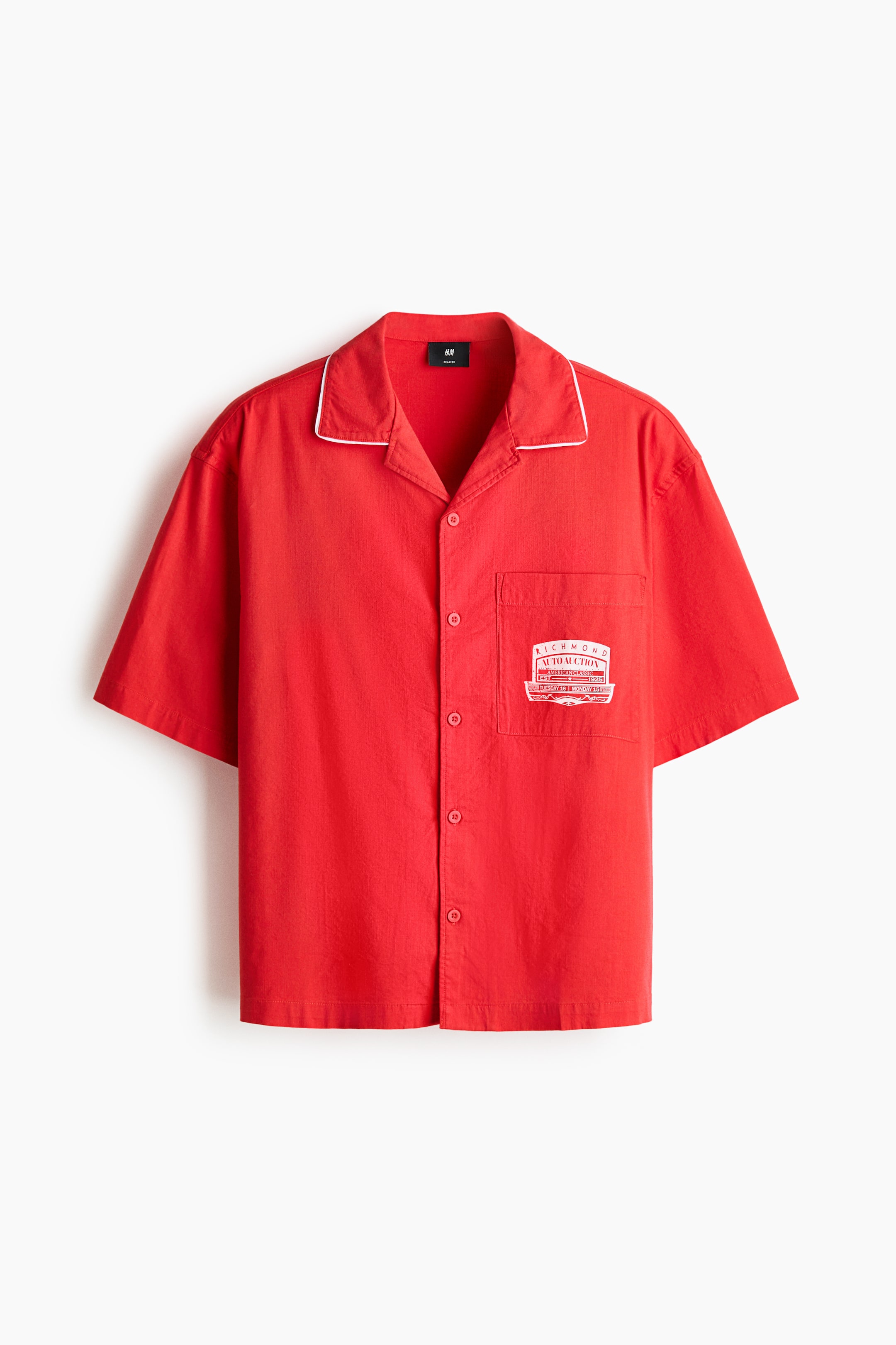 View larger image: A red short-sleeve shirt is shown from the front, featuring a revere collar with white piping and a button-front placket. A white graphic print appears on the single chest pocket.