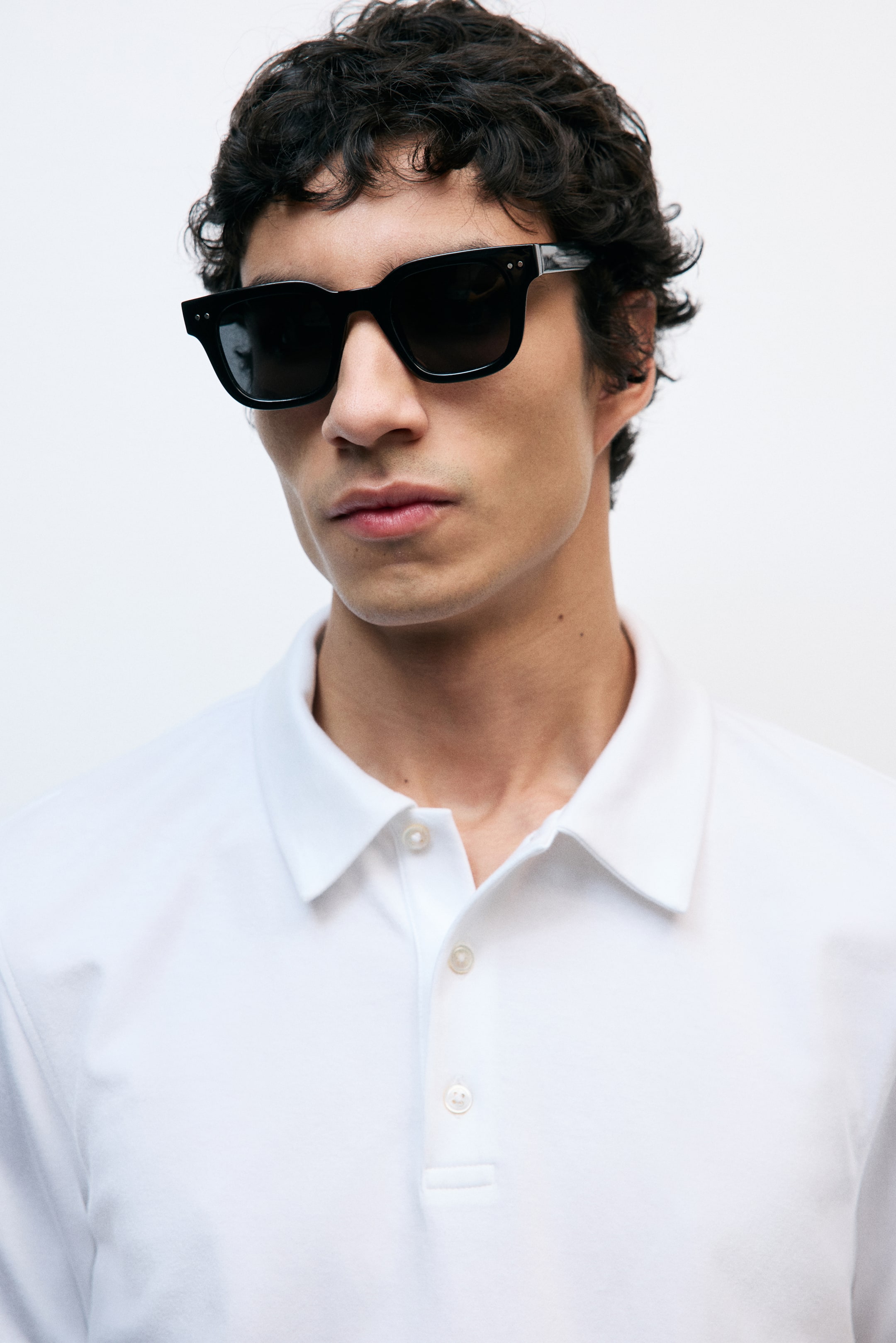 View larger image: Black rectangular sunglasses feature a thick frame with dark lenses, angled slightly to the right, showcasing two silver-coloured rivets on the front and a metallic detail on the right temple.