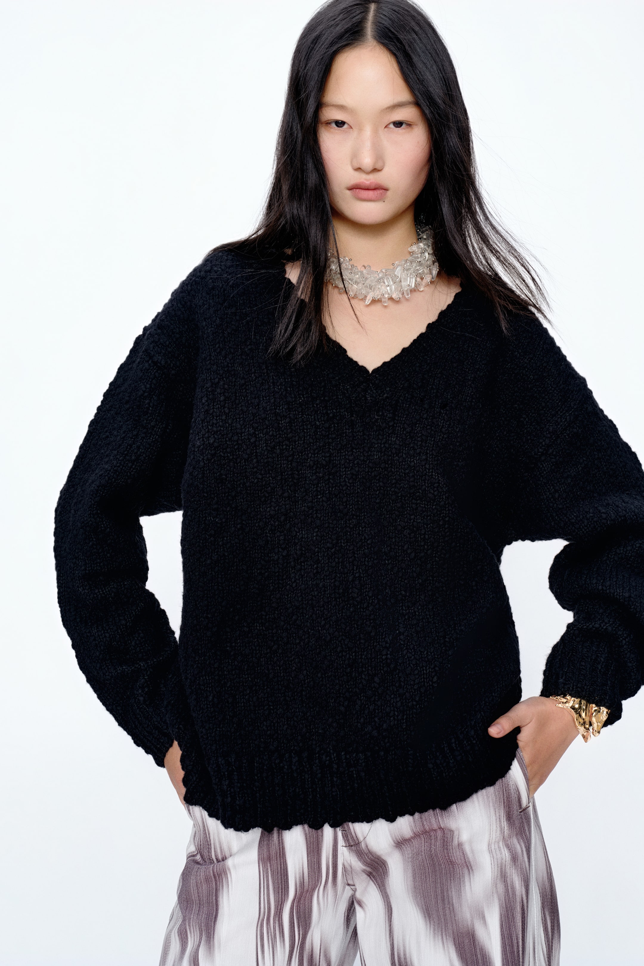 View larger image: A black V-neck sweater with a textured, chunky knit and a relaxed, slightly oversized fit, featuring long, voluminous sleeves gathered at ribbed cuffs and a ribbed ribbed hem.