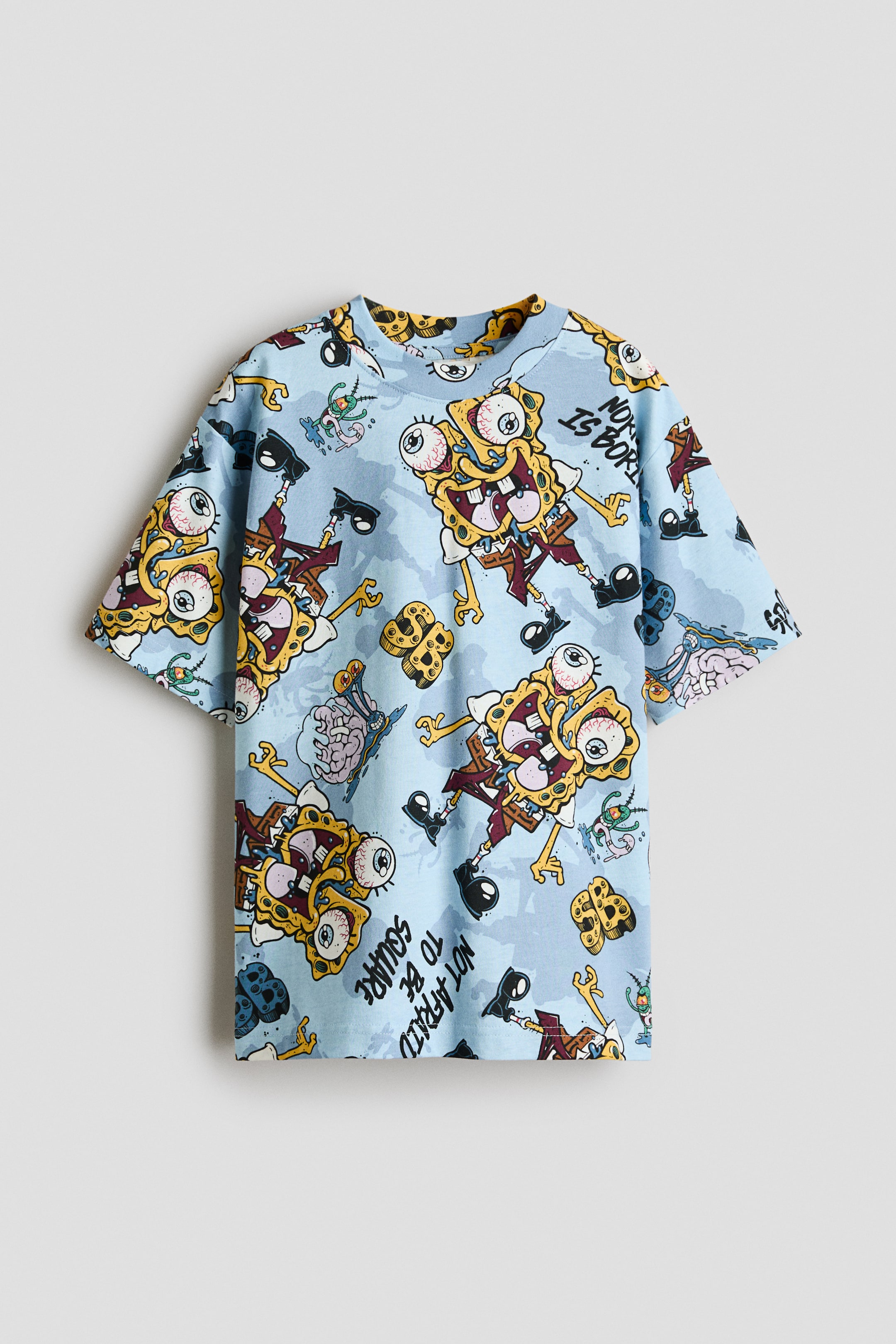 Ampliar la imagen: Esta camiseta de jersey de algodón azul claro se muestra de frente, con un estampado gráfico integral de un personaje de caricatura. Está diseñada con un escote redondo con ribete acanalado y hombros caídos de corte relajado.