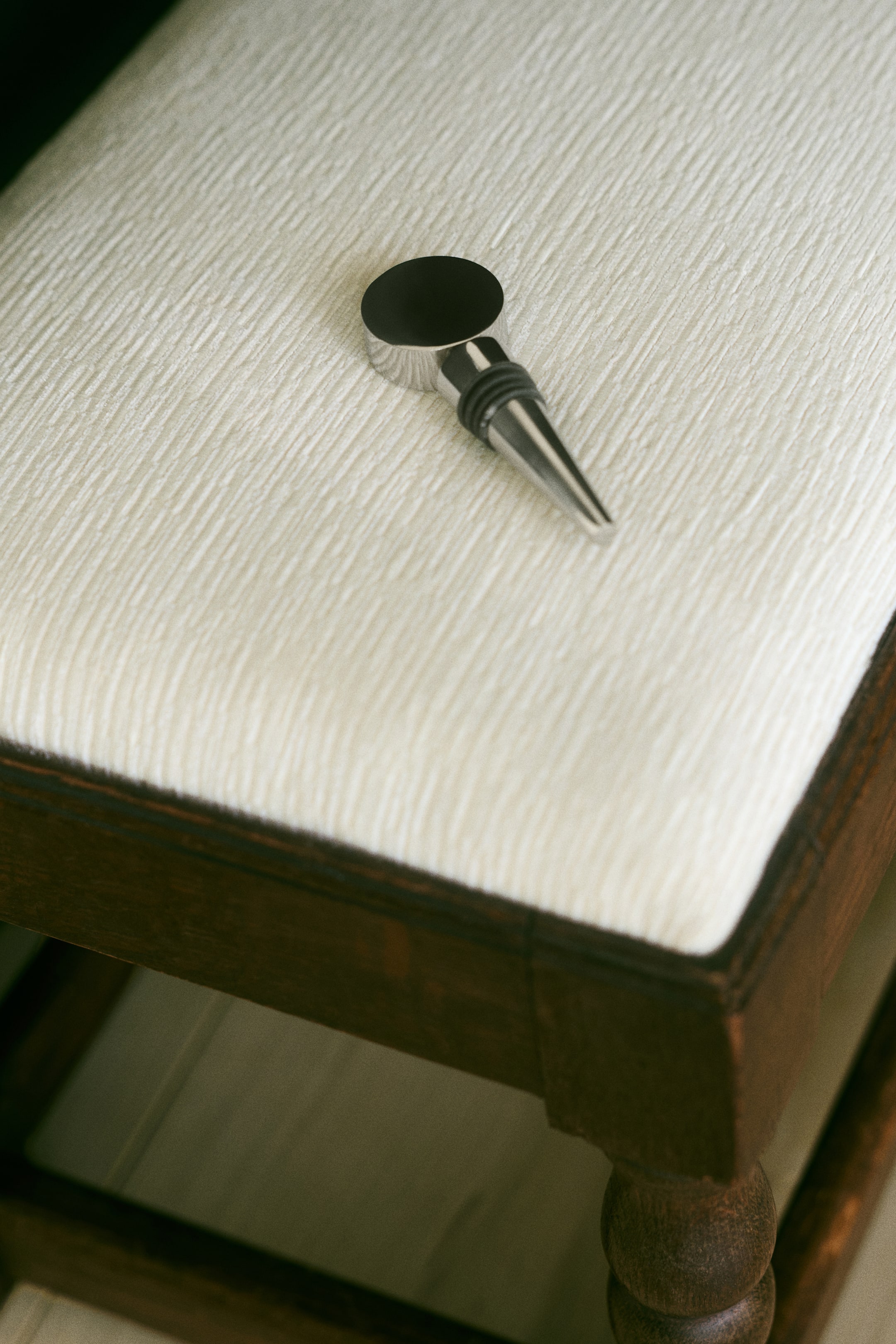 View larger image: A bottle stopper in polished stainless steel is resting on its side, showcasing a flat, circular geometric top with a black insert and a tapered metal body featuring black rubber sealing rings.