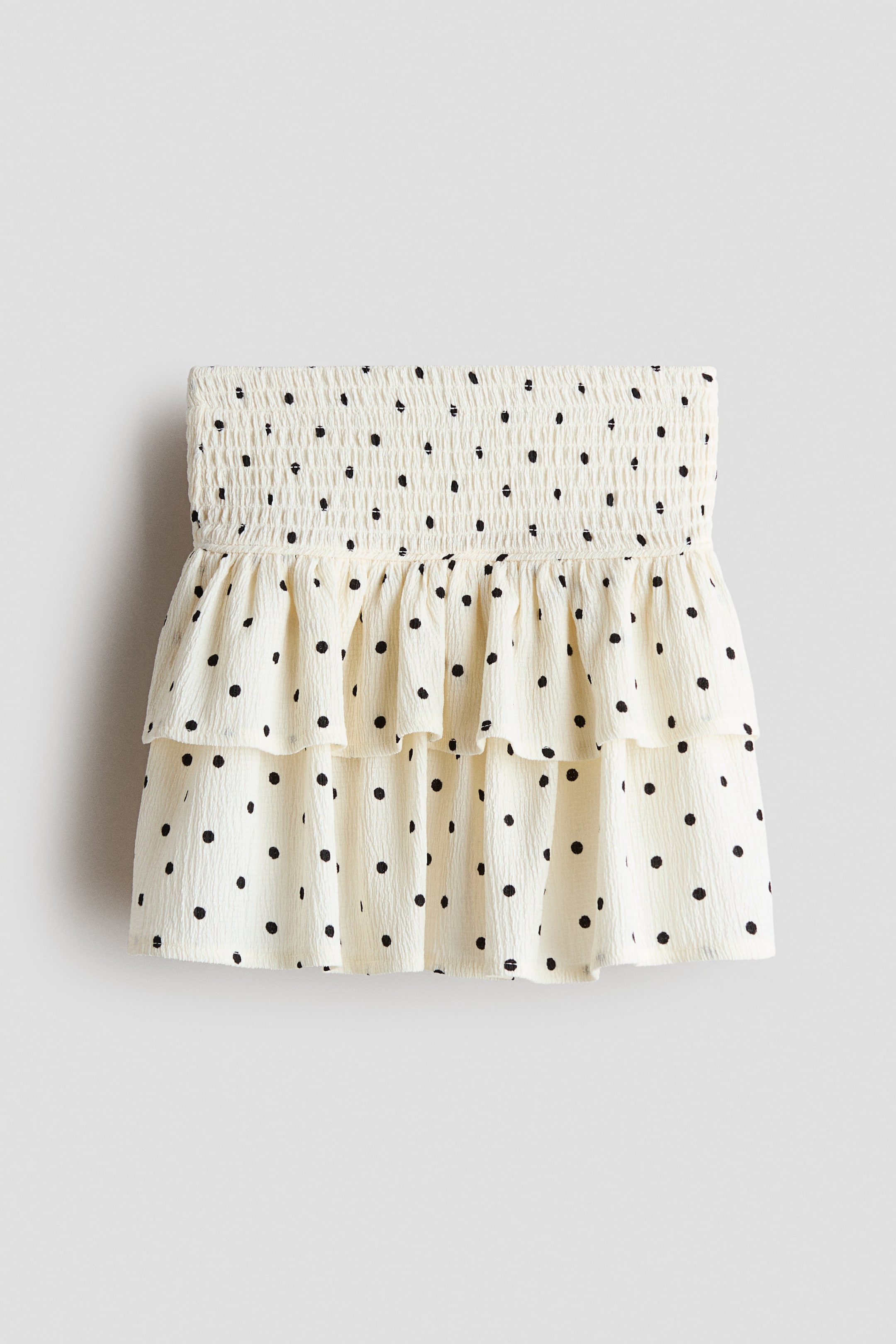 Ingrandisci l'immagine: Una gonna a balze in jersey stropicciato con fascia in vita arricciata, base color crema con pois neri e due balze arricciate.