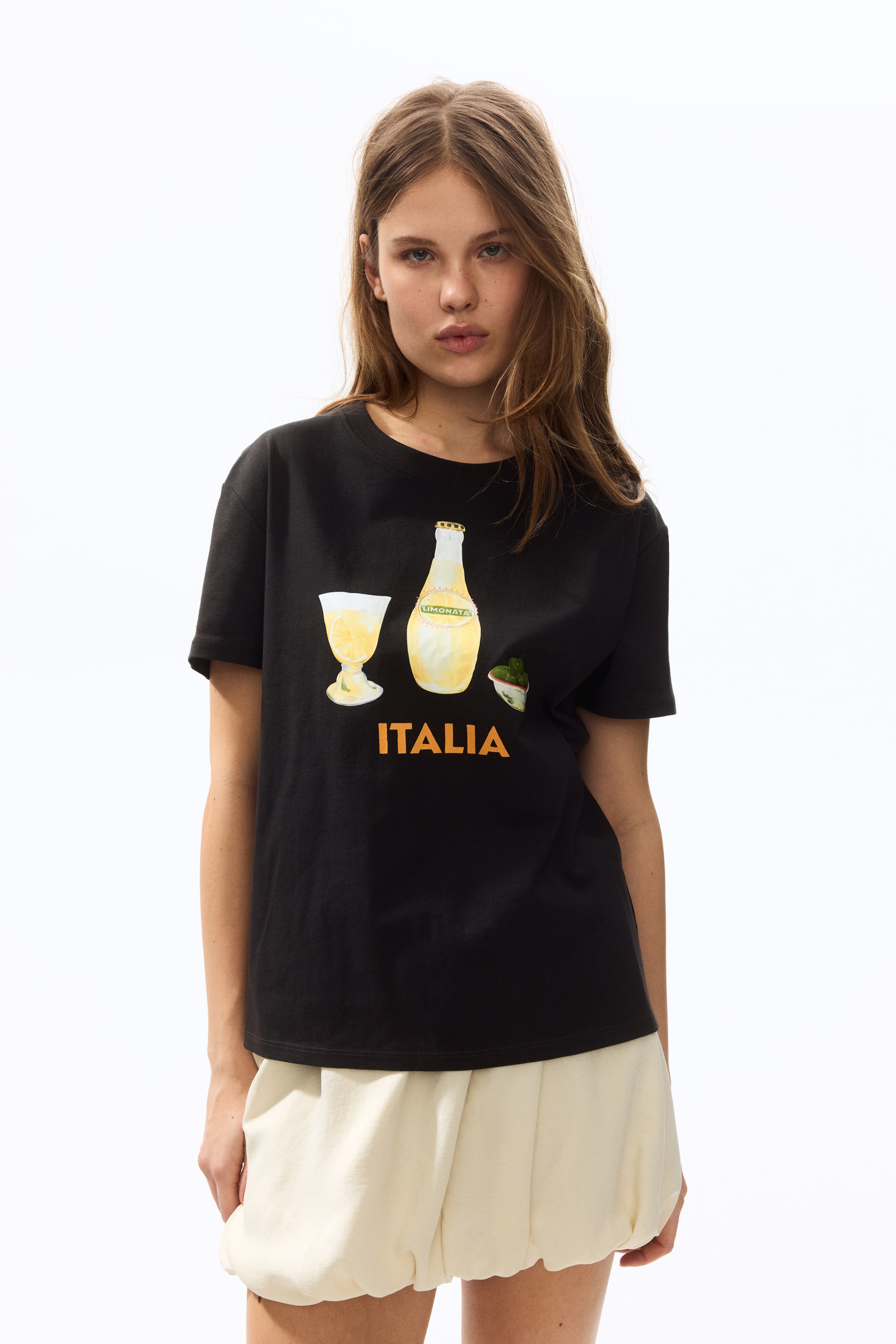 View larger image: A black t-shirt featuring a crew neck and short sleeves, with a front graphic print showcasing a glass filled with yellow liquid, a "Limonata" bottle, a small bowl with green items, and the word "ITALIA" in bold orange capital letters.