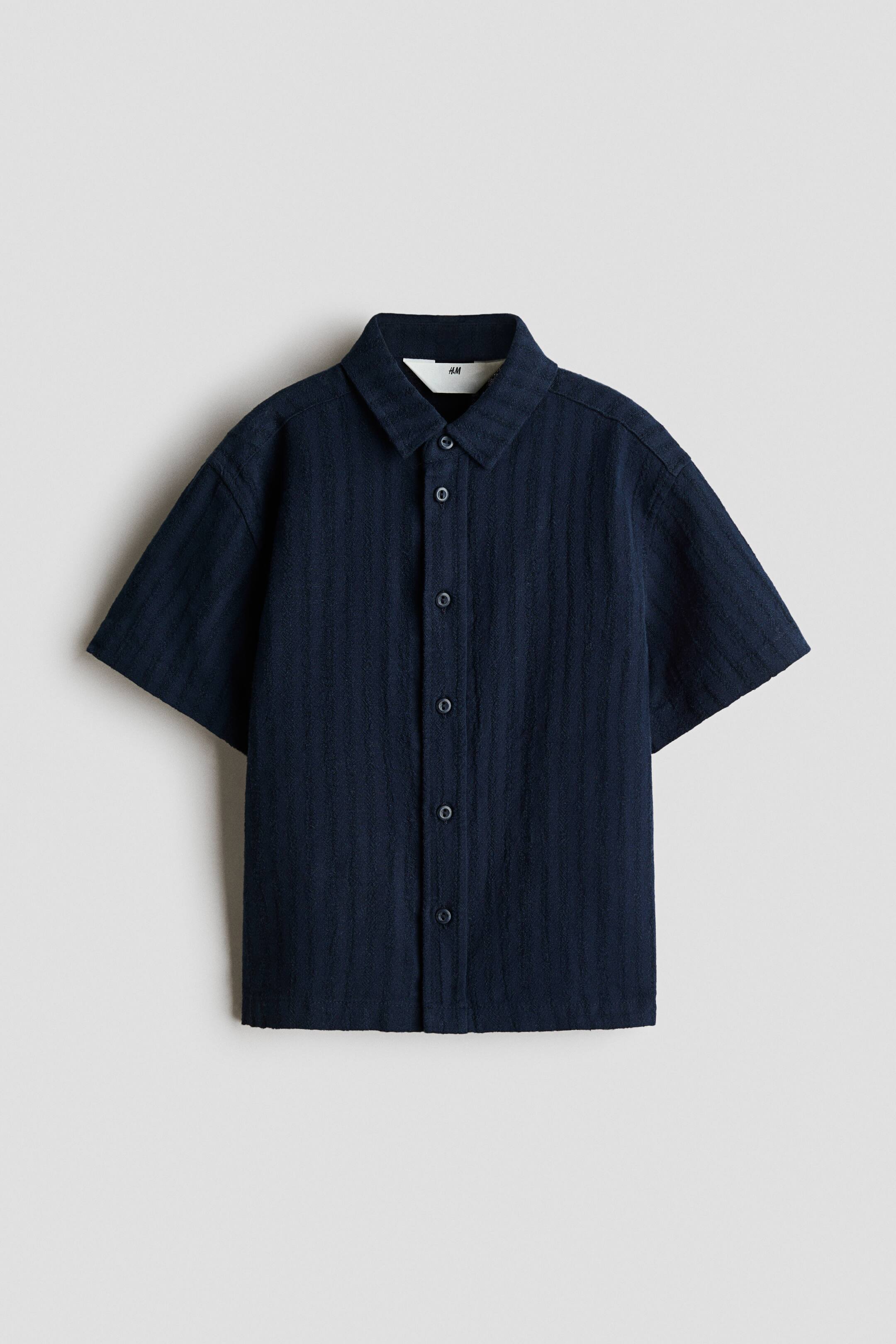 View larger image: A dark navy blue short-sleeve shirt is shown from the front, featuring a textured vertical ribbed pattern and a classic point collar. It is detailed with a front button placket and wide-cut, relaxed sleeves.