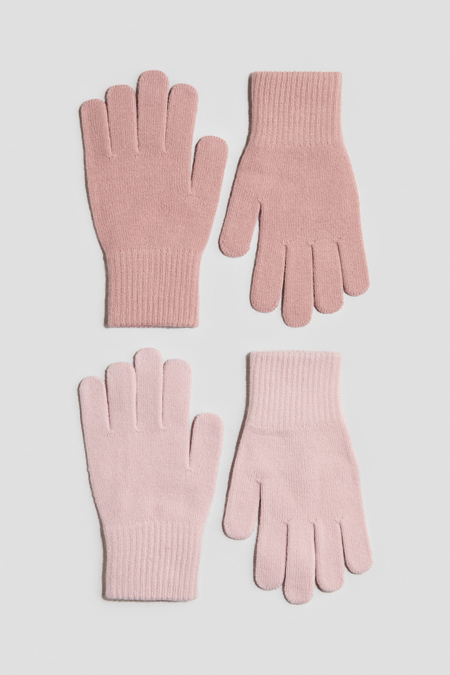 Dos pares de guantes de tejido fino y suave están colocados planos, de frente, y muestran un par en rosa empolvado y otro en rosa claro. Ambos pares presentan un diseño clásico de cinco dedos con puños acanalados.