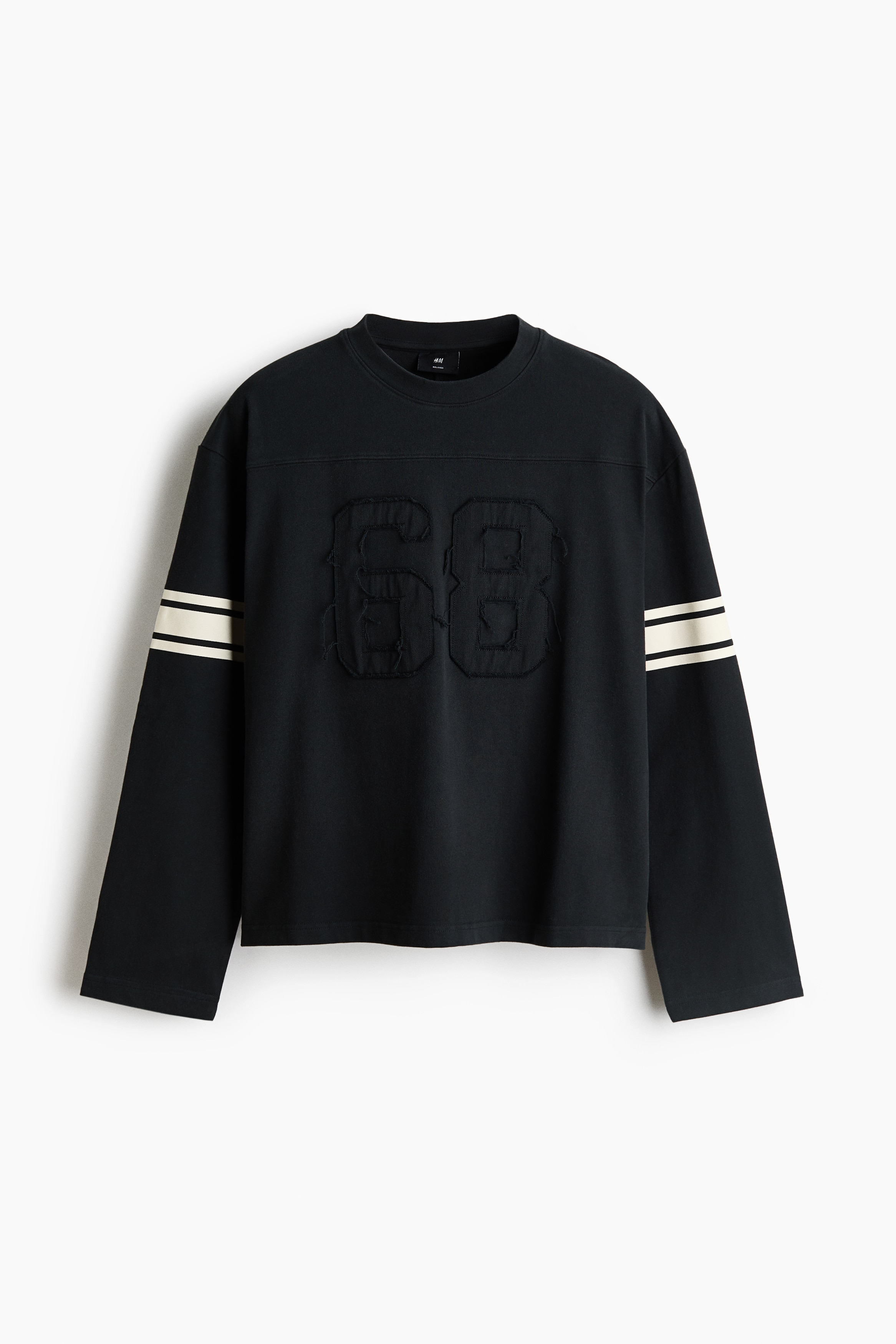 Una blusa negra de manga larga y cuello redondo se muestra de frente, con un aplique tonal deshilachado del nÃºmero "68" en el centro del pecho. La prenda estÃ¡ diseÃ±ada con hombros caÃ­dos, un ajuste relajado y dos franjas contrastantes color blanco roto que rodean cada manga superior.
