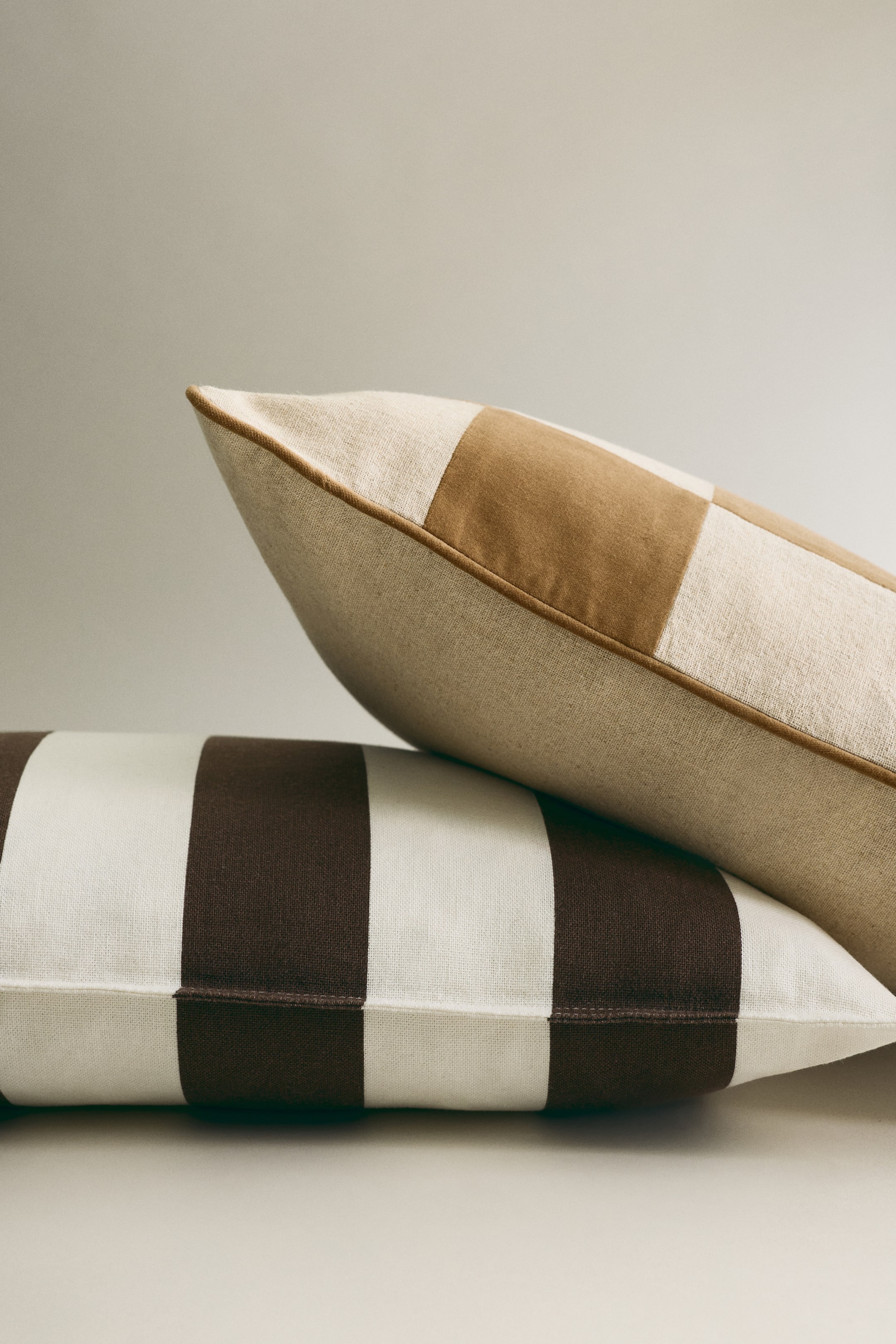 Преглед на по-голямо изображение: Декоративна възглавница с каре в светло бежово и кафяво и кафяв кант е поставена под наклон върху втора възглавница, която е с широки светло бежови и кафяви райета.