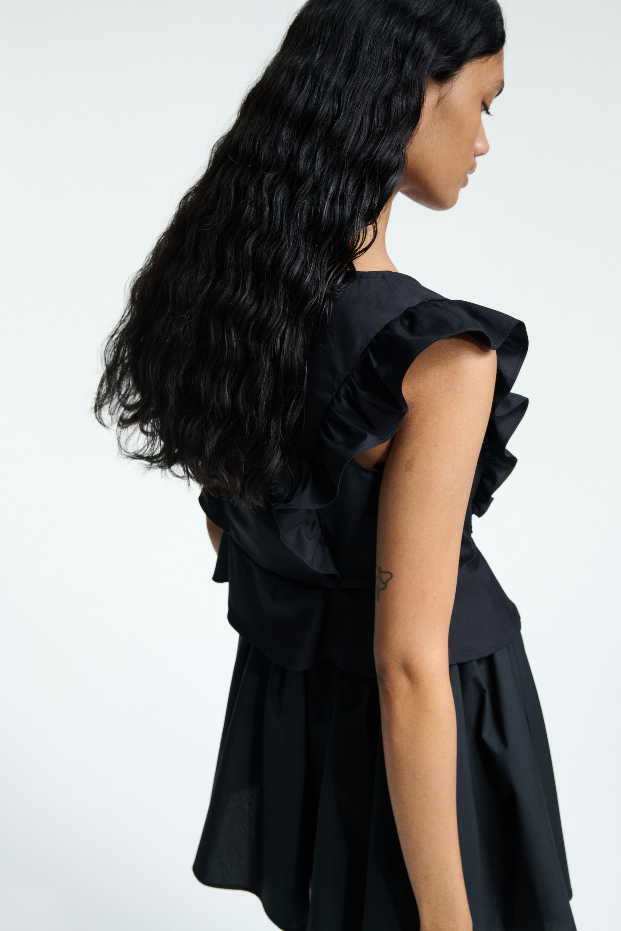 View larger image: A black top and a gathered, flared bottom are being presented from the back-right side. The top is designed with ruffled cap sleeves and a layered, ruffled back.