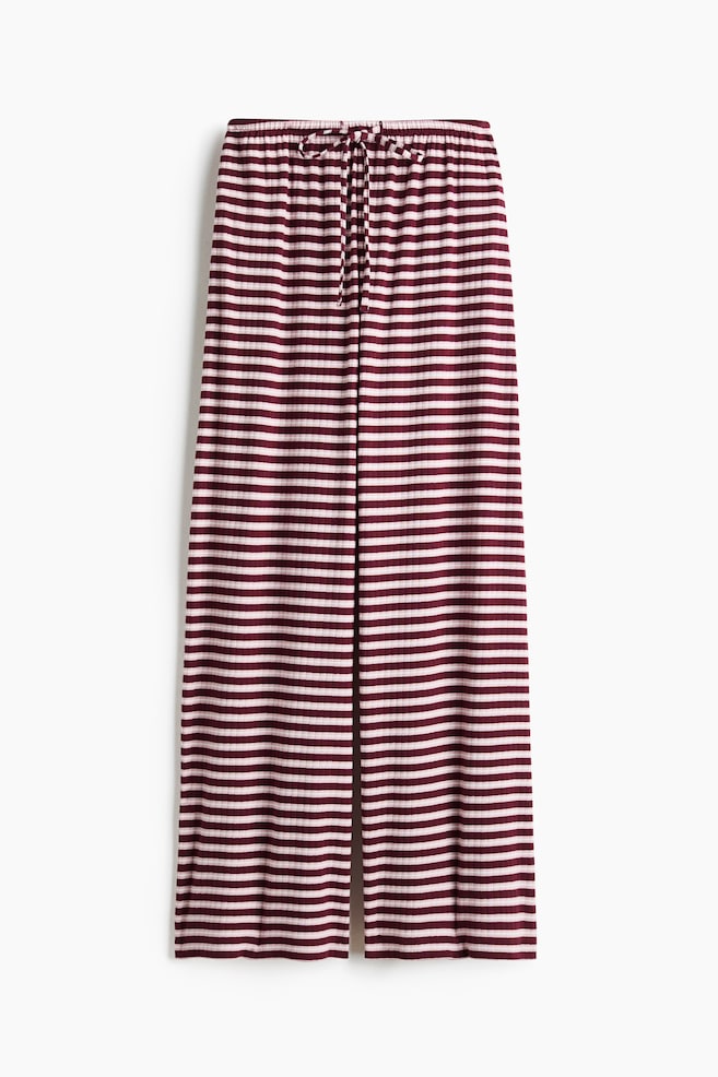 Loose-fit trousers in ribbed cotton jersey are shown from the front, featuring a burgundy and off-white horizontal striped pattern. The trousers have a wide-leg silhouette and an elasticated waistband with a matching drawstring tied at the centre. - 1