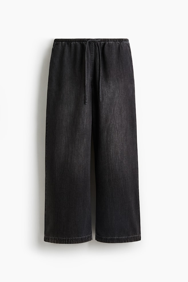 Les pantalons amples à coupe droite sont présentés dans un denim foncé, avec des jambes larges. La taille présente une élastication recouverte et un cordon de serrage visible. - 1