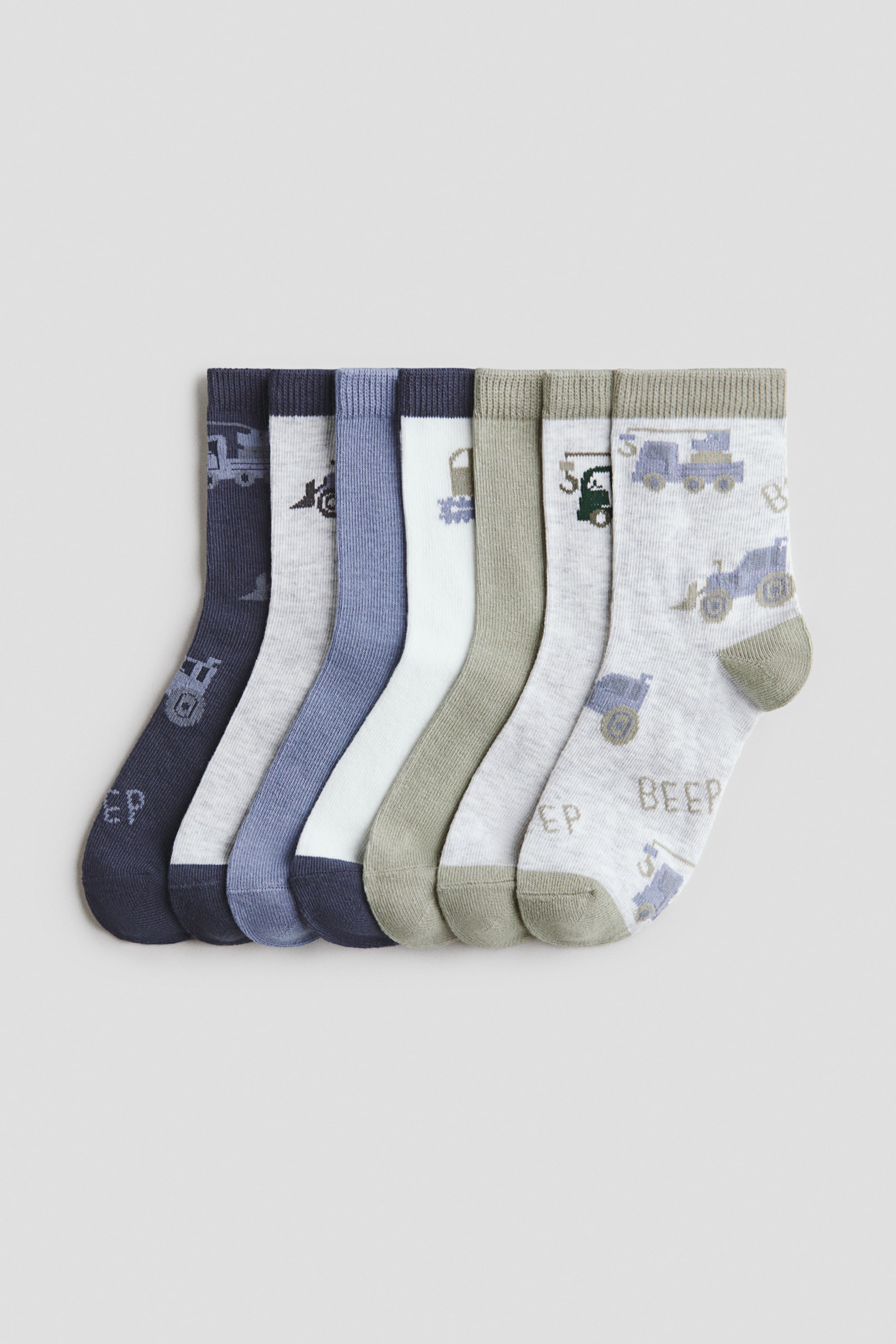 View larger image: "Socks crafted from a soft, fine knit cotton blend with elasticated tops are elegantly arranged in a fan-like display, highlighting their fronts. They boast ribbed cuffs and come in a variety of colours and patterns featuring construction vehicles and the text 'BEEP'."
