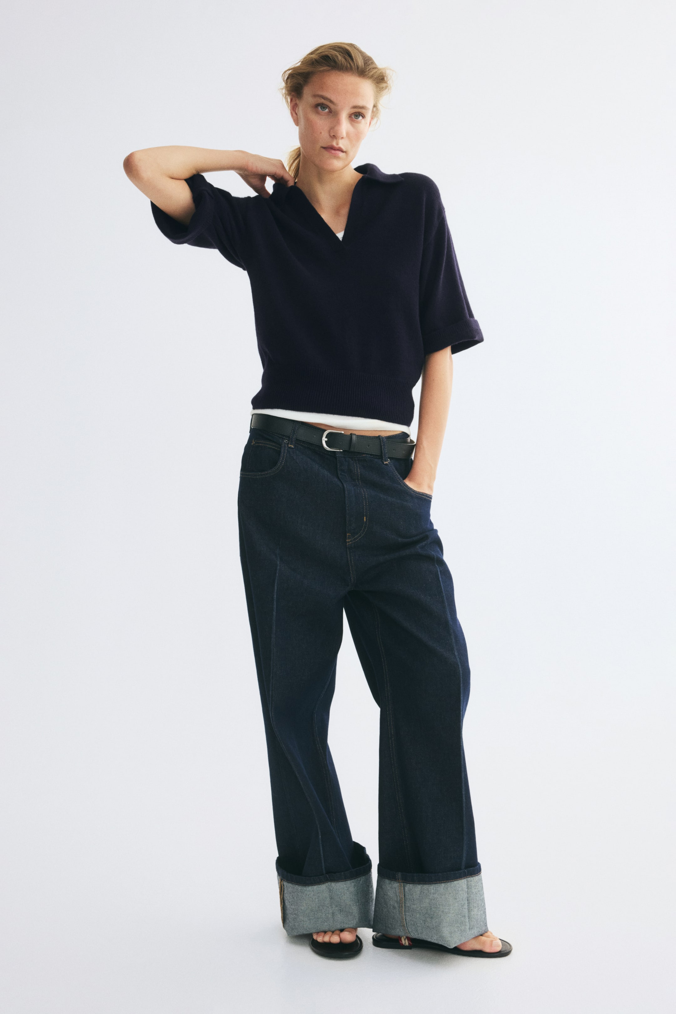 Voir une image plus grande: Un polo en tricot fin bleu marine foncé est présenté de face, avec un col ouvert, des épaules tombantes et des manches longueur coude avec poignets côtelés. Le polo affiche un ourlet côtelé et est superposé sur un T-shirt blanc qui dépasse au niveau de l’encolure et de la taille.