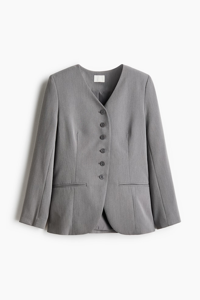 A grey, lapelless twill blazer is shown from the front, featuring a V-neckline, a six-button front closure, and front waist darts. The relaxed-fit blazer features horizontal jetted pockets, long sleeves, and a curved hemline. - 1