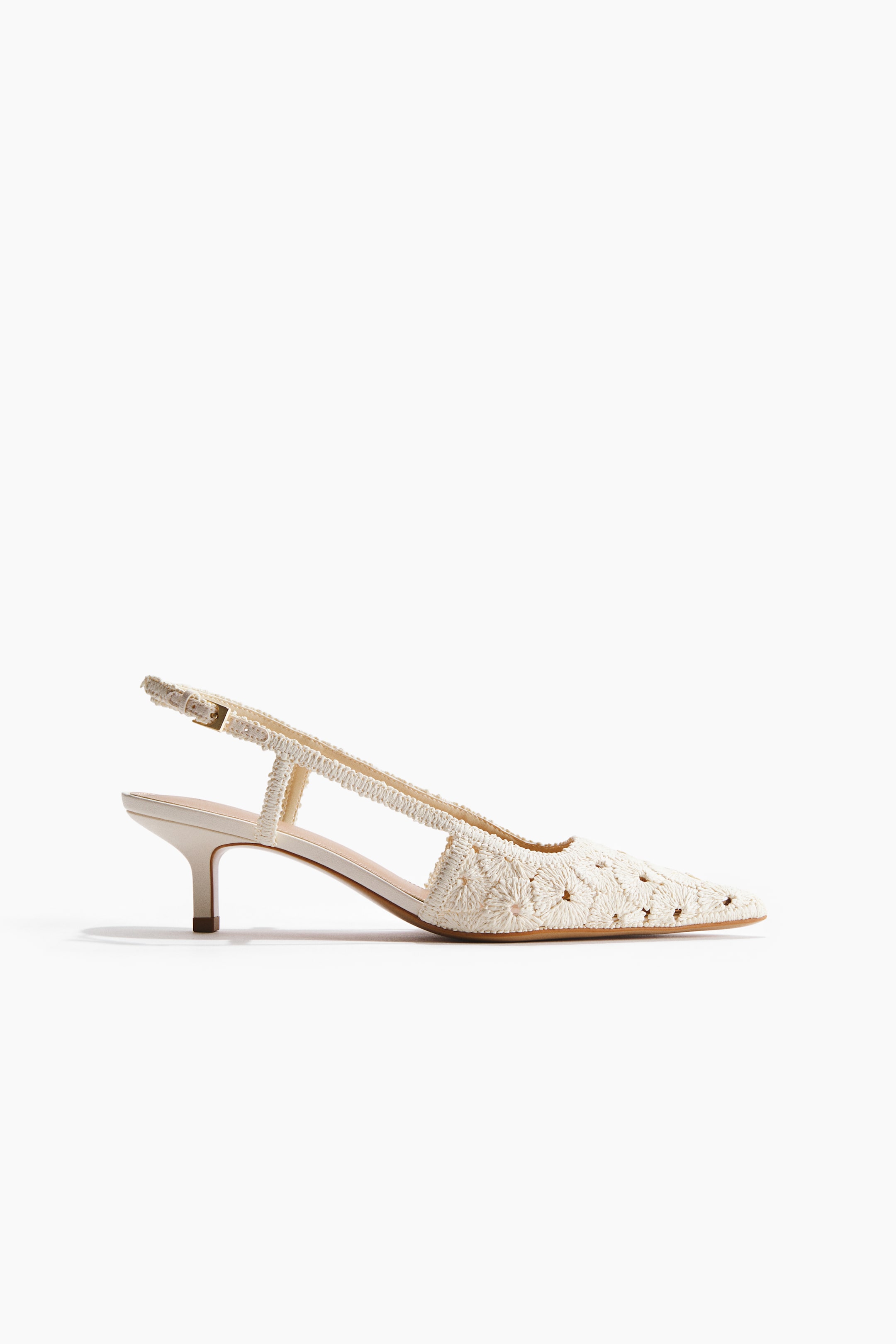 View larger image: A cream-coloured slingback shoe featuring a pointed toe, a kitten heel, and a narrow, adjustable ankle strap with a metal buckle. The shoe's upper displays intricate crocheted floral patterns.
