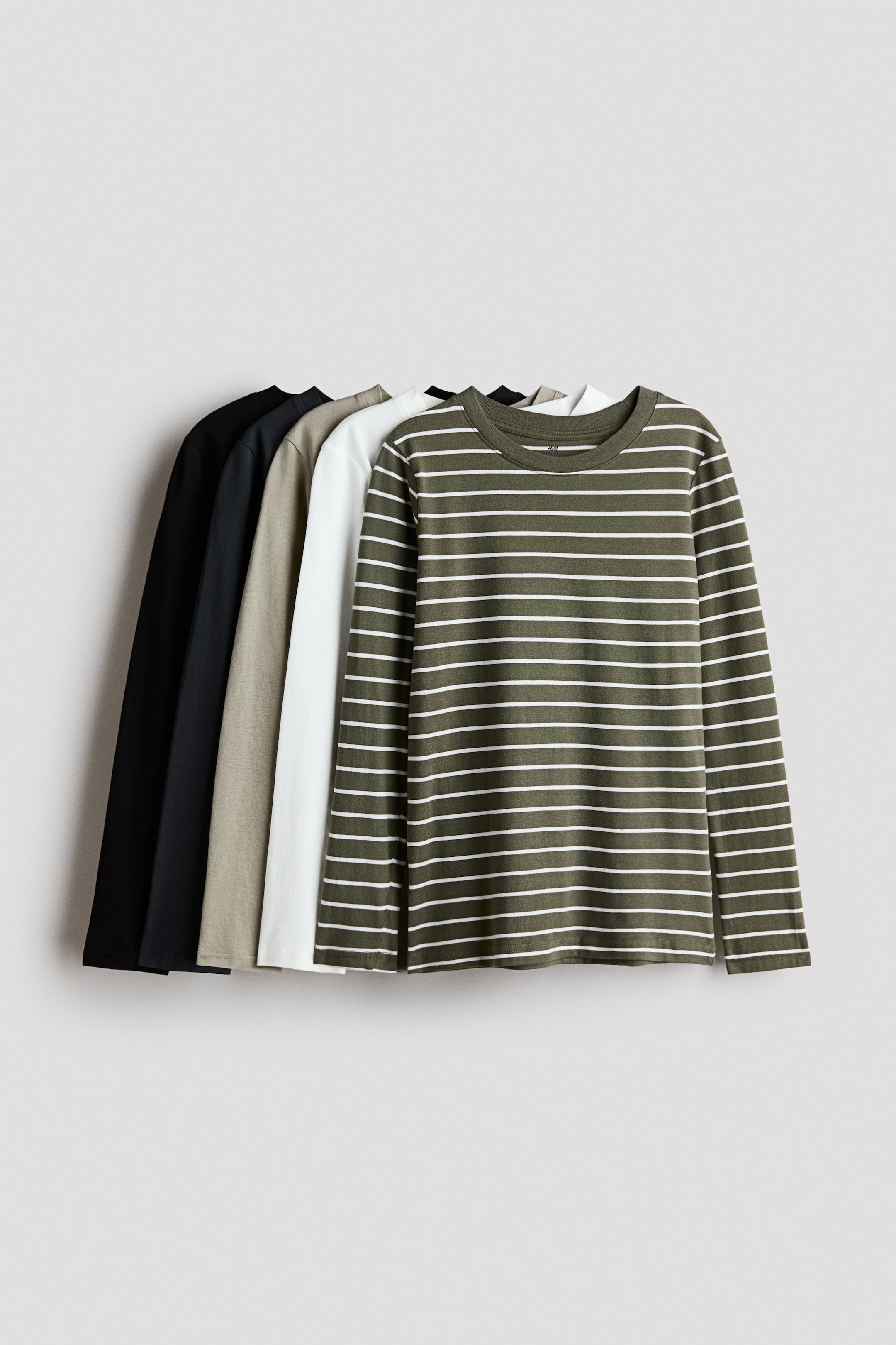 View larger image: Five long-sleeve cotton jersey T-shirts are hanging in a staggered, overlapping row facing forward, with the front-most shirt displaying an olive green and white horizontal striped pattern. The remaining shirts layered behind are in solid white, khaki, dark gray, and black, all featuring a round, rib-trimmed crew neckline.