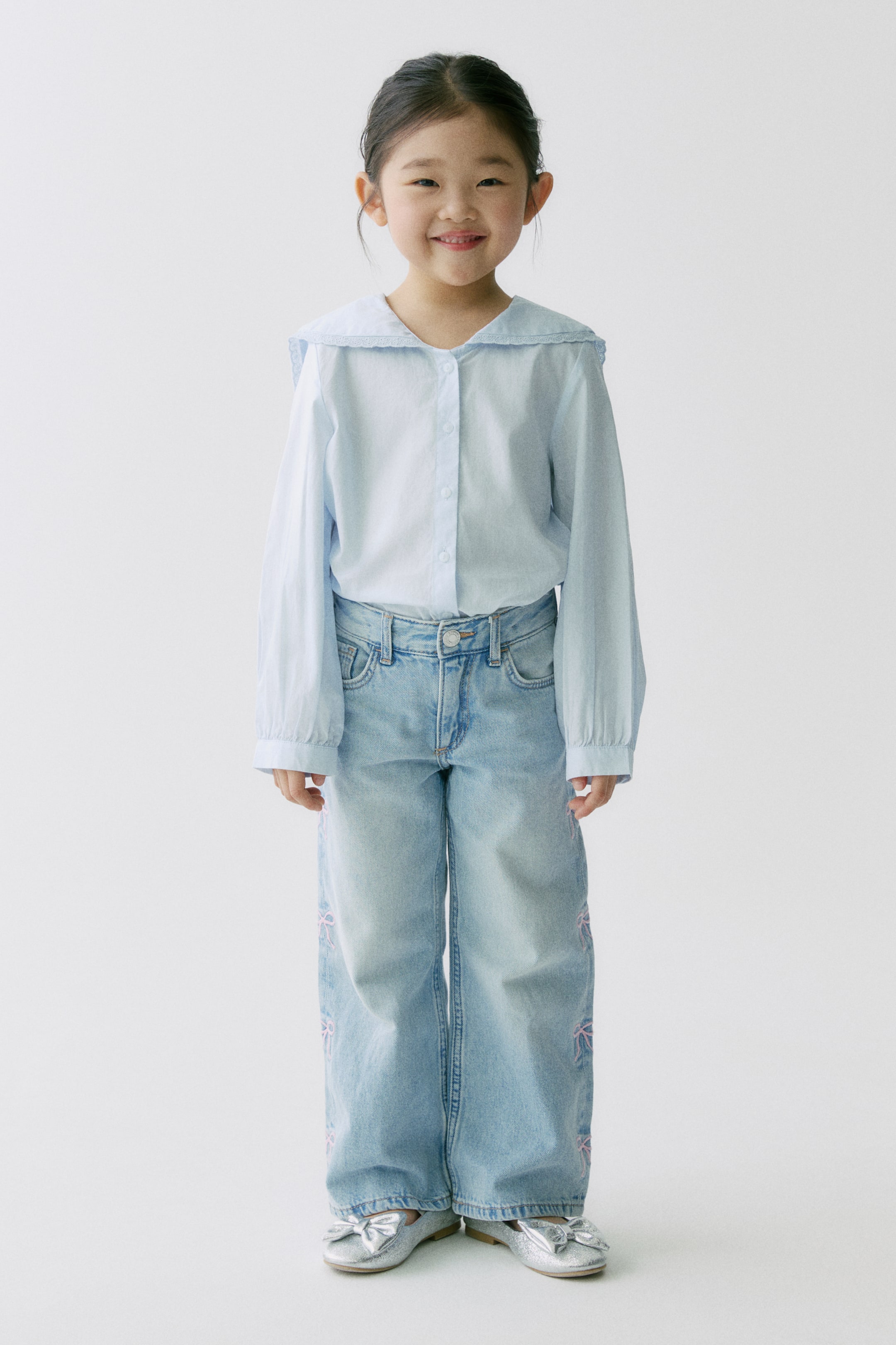 查看大圖: 這件淺藍色上衣採用柔軟棉質織法製成，配有雙層蕾絲滾邊的水手領，前襟並設有排釦。模特兒穿著該上衣，長袖設有帶鈕扣的袖口。