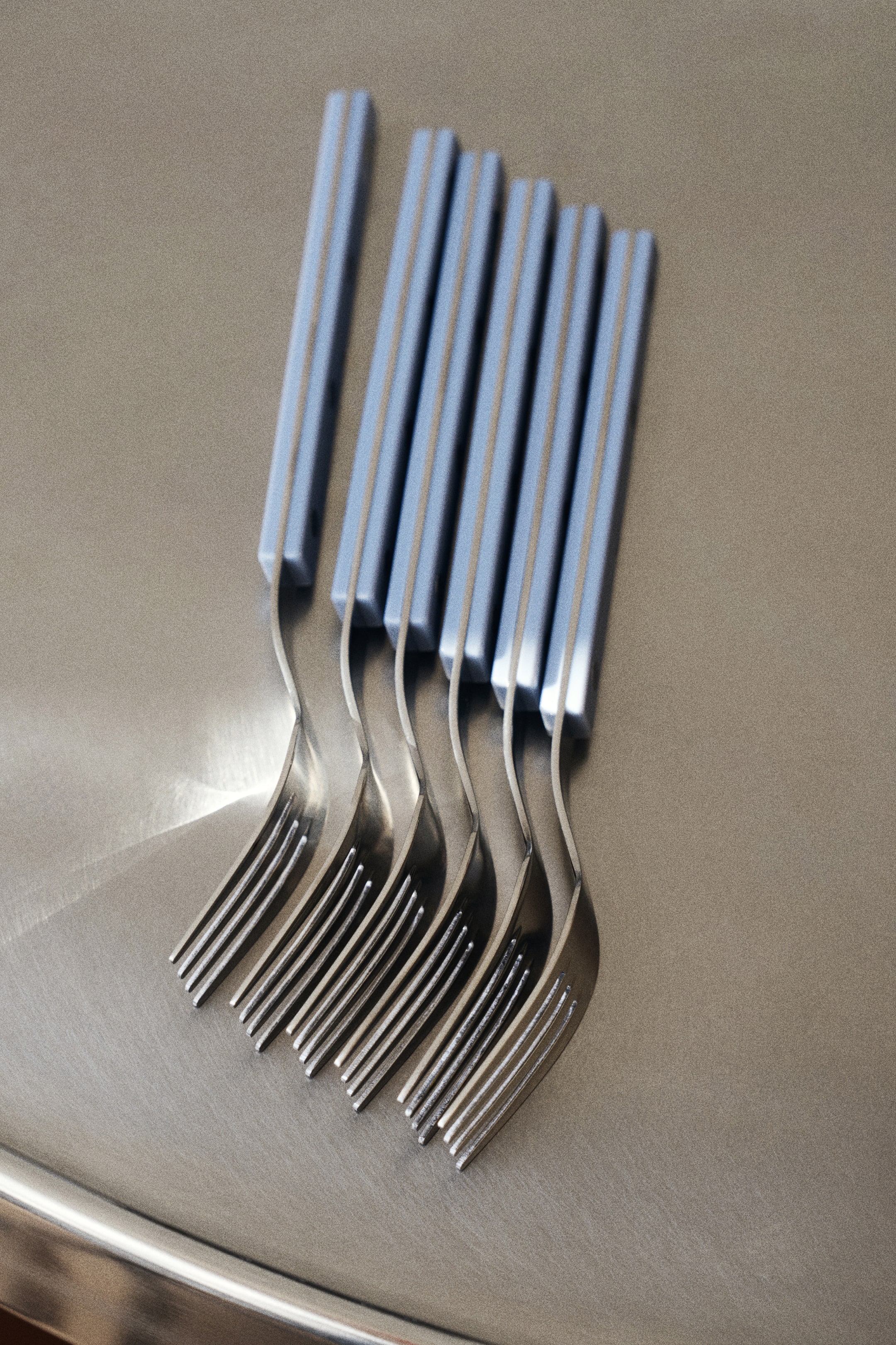 Agrandir l'image: Plusieurs fourchettes en acier inoxydable présentent des manches rectangulaires bleu clair. Les fourchettes sont disposées en formation décalée, avec leurs manches orientés vers le haut et leurs dents courbées vers le bas à gauche.