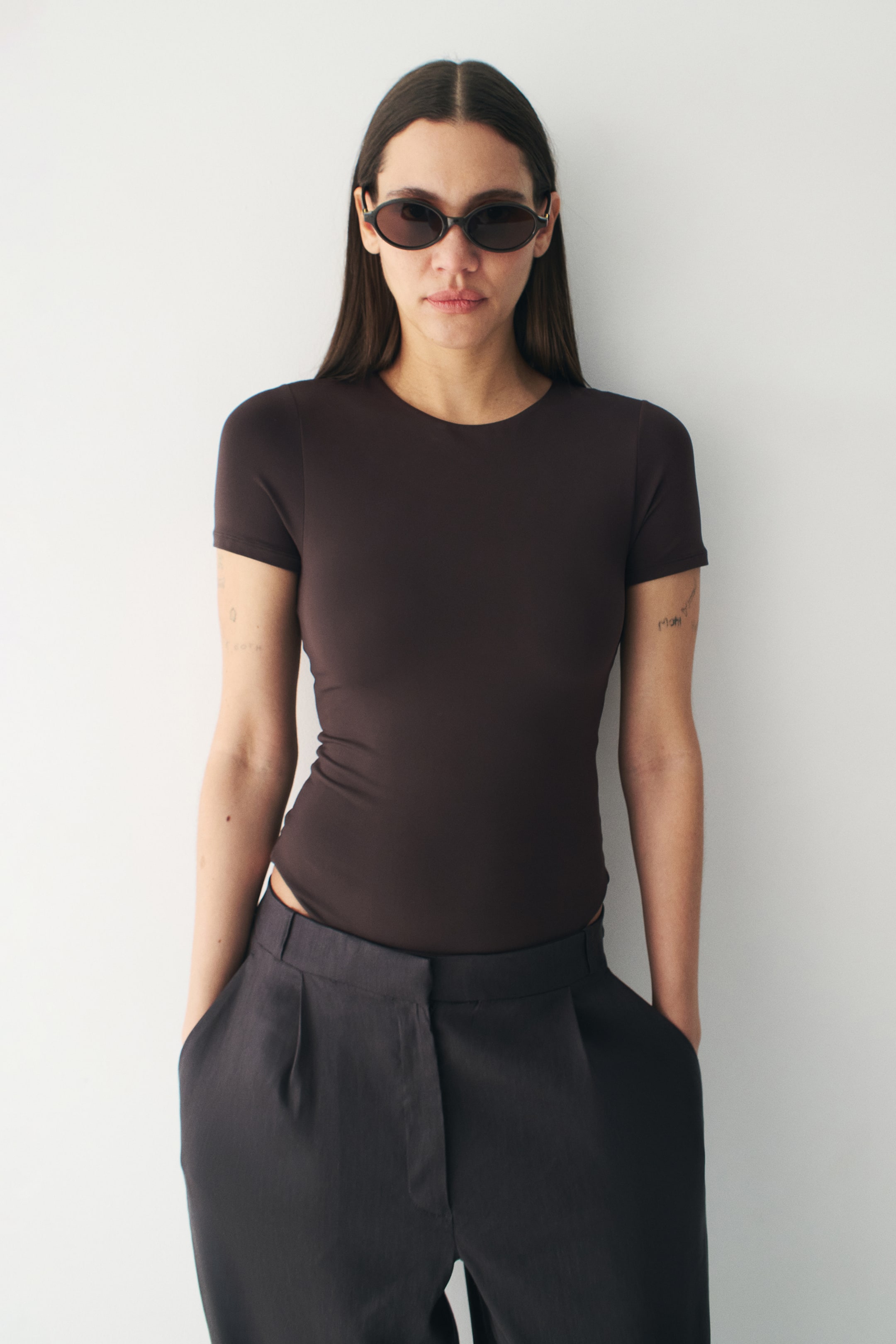 Ingrandisci l'immagine: Un body a maniche corte di colore marrone scuro presenta una silhouette aderente con scollo rotondo e una texture liscia.