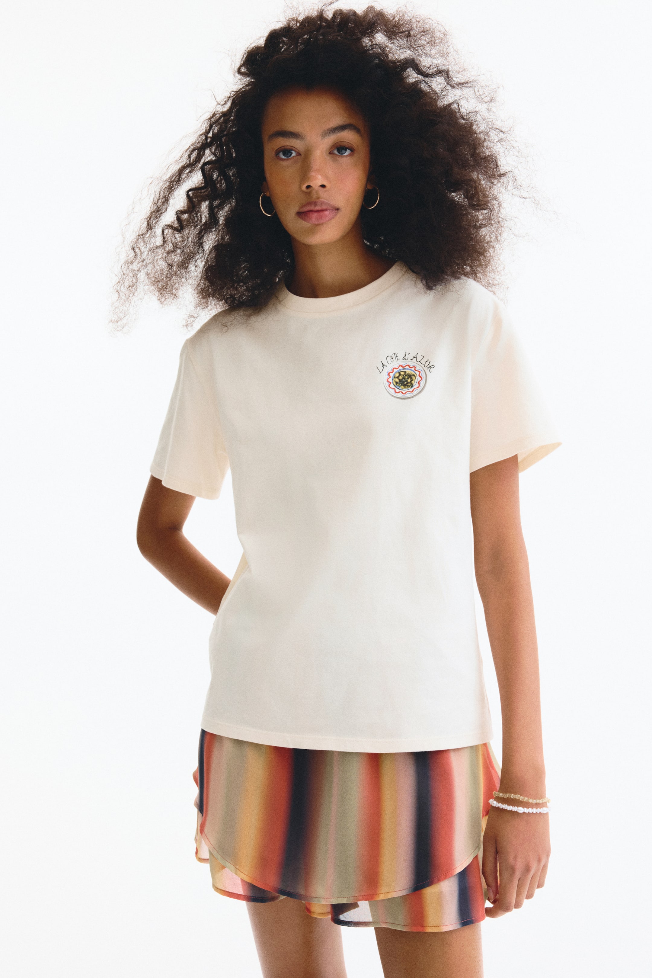 View larger image: Presenting a cream-colored t-shirt with a crew neck and short sleeves. On the left chest, there's a circular graphic showcasing a plate of pasta with the text 'LA CÔTE D'AZUR' above it.