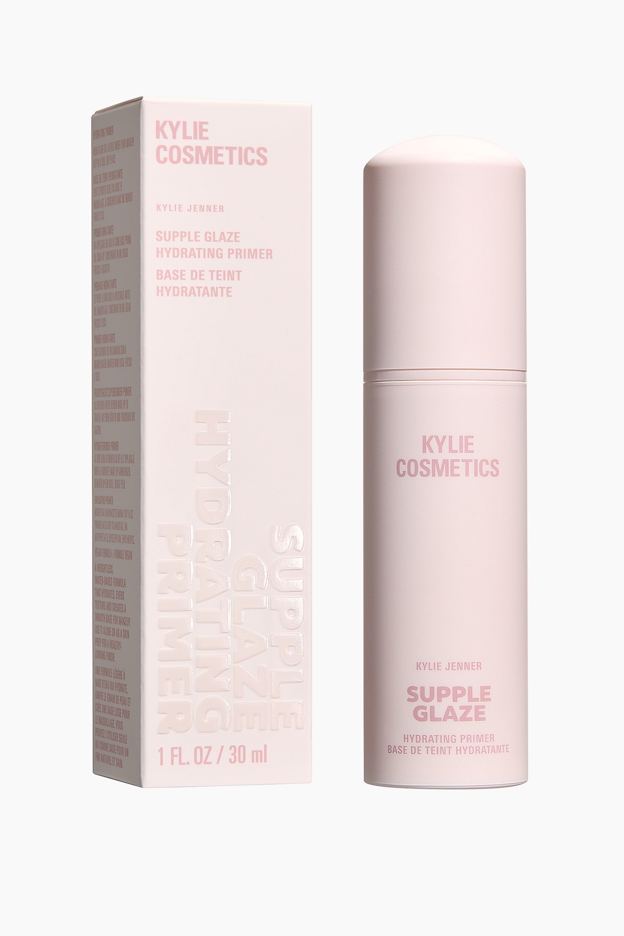 Visa större bild: Den ljusrosa lådan för Kylie Cosmetics Supple Glaze Hydrating Primer står lutad något åt vänster, vilket visar dess framsida och vänstra sida, medan den matchande cylindriska flaskan står upprätt, vänd framåt. Både lådan och flaskan visar 'Kylie Cosmetics', 'Kylie Jenner', 'Supple Glaze', 'Hydrating Primer' och 'Base de Teint Hydratante' på sina framsidor; lådan visar även '1 FL. OZ / 30 ml' och präglad text, inklusive 'Supple Glaze Hydrating Primer', som löper vertikalt längs dess synliga vänstra sida, och flaskan har en synlig söm runt dess mitt.